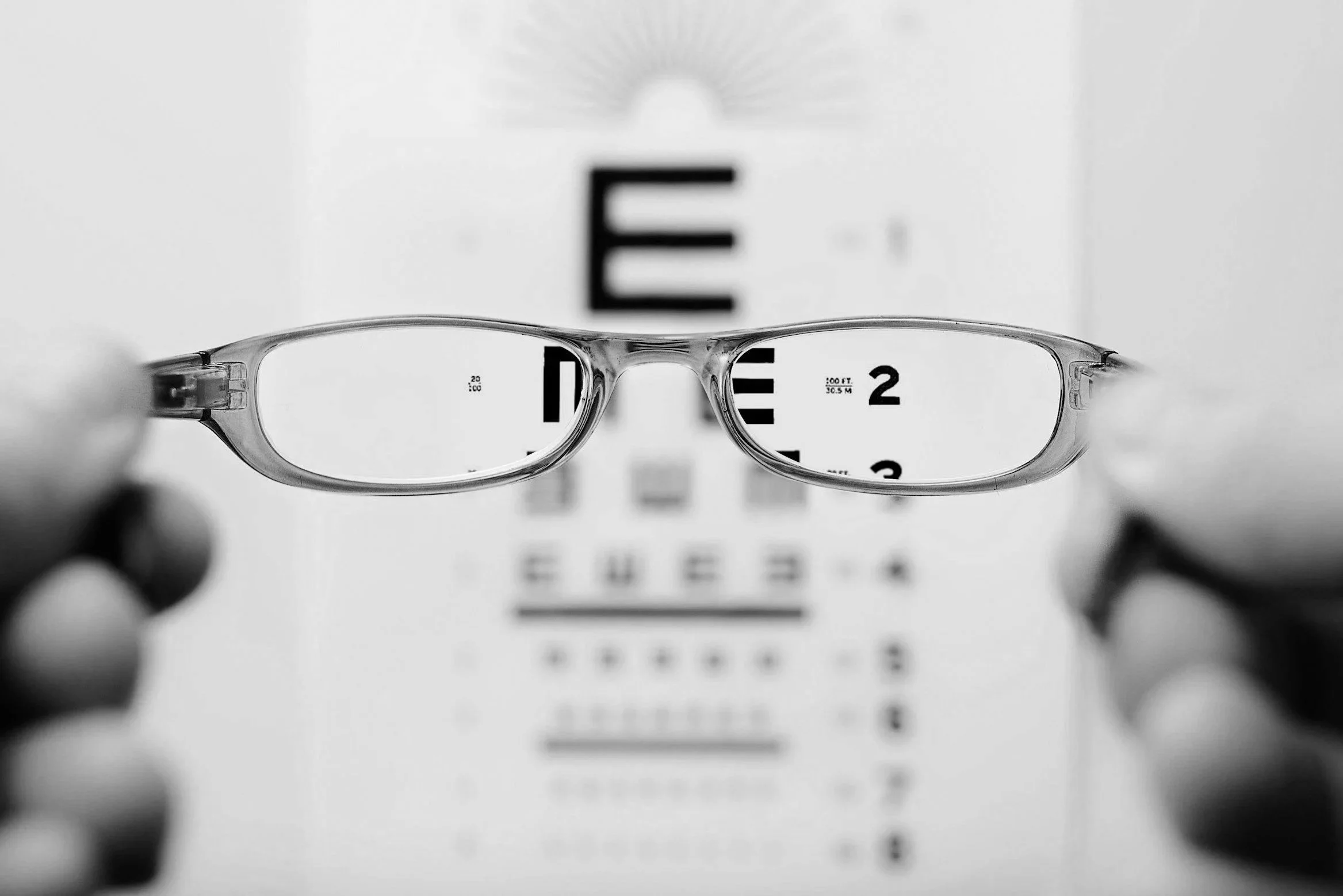 Eyeglasses held in front of an eye chart, showing the letters through the lenses.