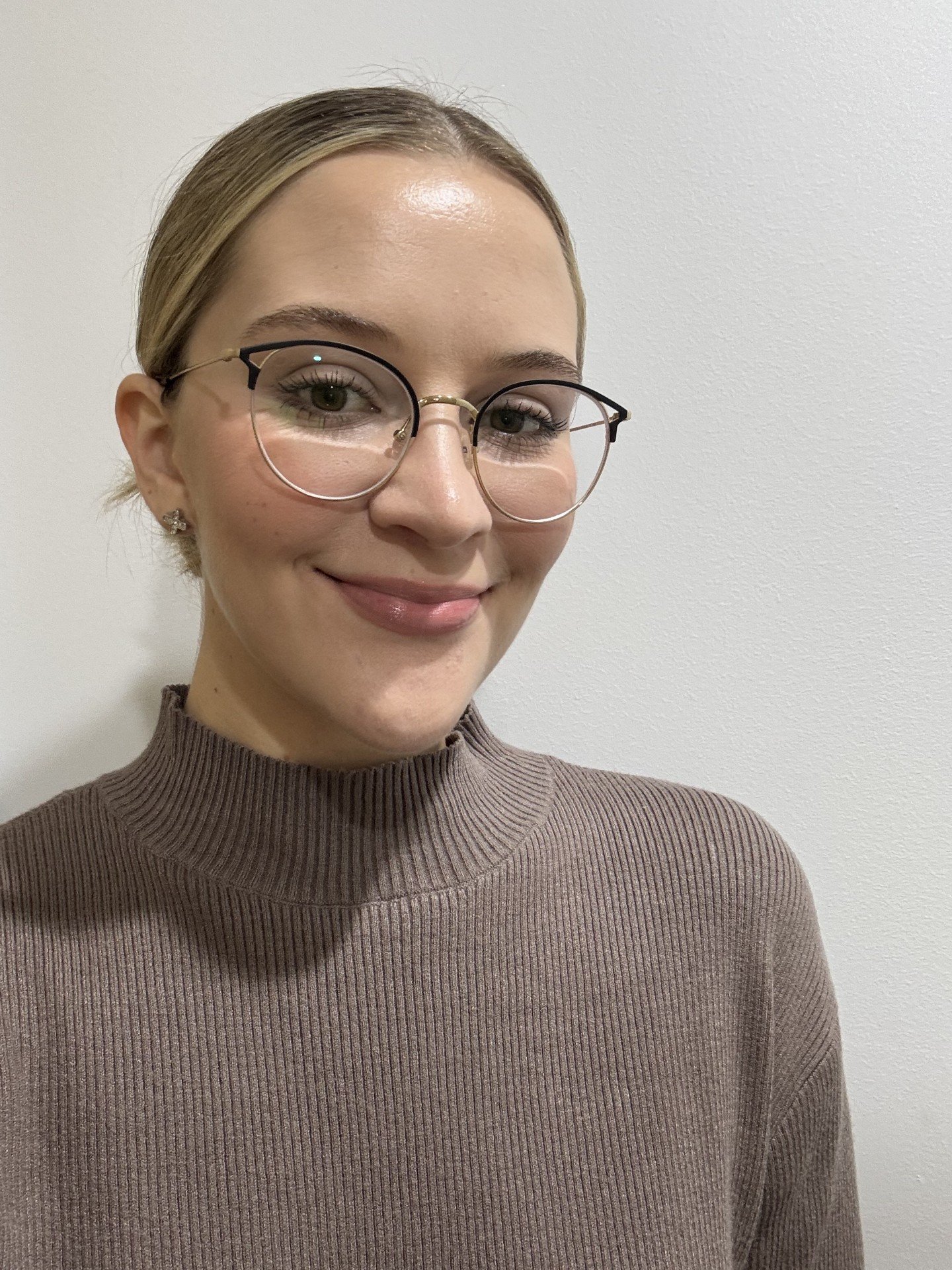 A woman with blonde hair and glasses smiling in front of a plain white wall.