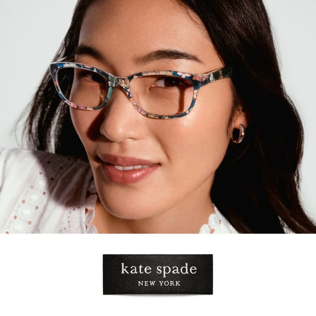 A woman with dark hair and earrings wearing colorful patterned glasses, smiling, with the Kate Spade New York logo below.