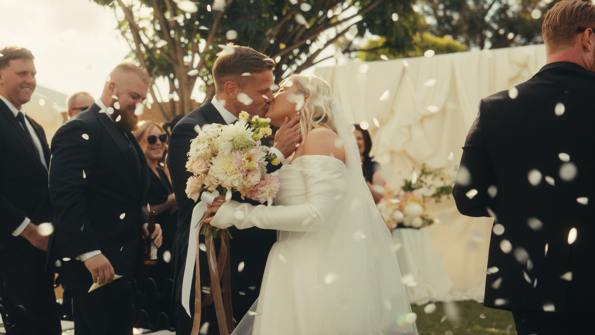 A bride and bridesmaids smiling with trees and sunlight in the background.