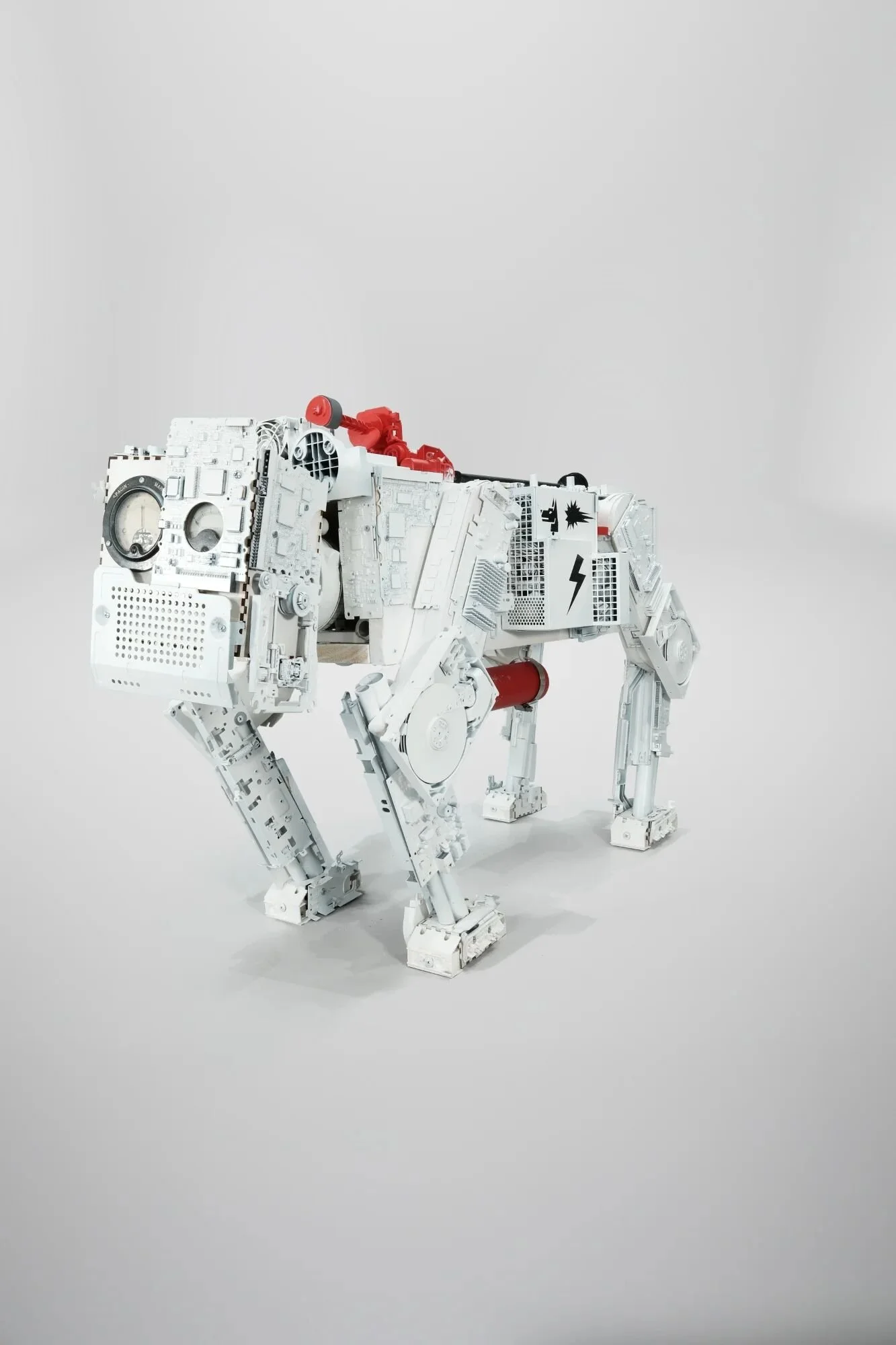 Death-white SPOT reconstruction. Boston Dynamics surveillance robot rebuilt from e-waste and salvaged materials. Montana Shock White coating over hard drives, circuit boards, RAM. Shock Red accents signal dormant Friday transformation. Stands 5° from