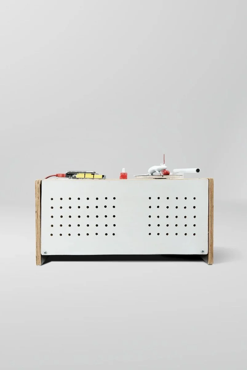 White laboratory mouse glued permanently to inescapable wheel, chasing red marble it can never reach. Mouse spins faster as volume increases—mechanically proven, not metaphorical.