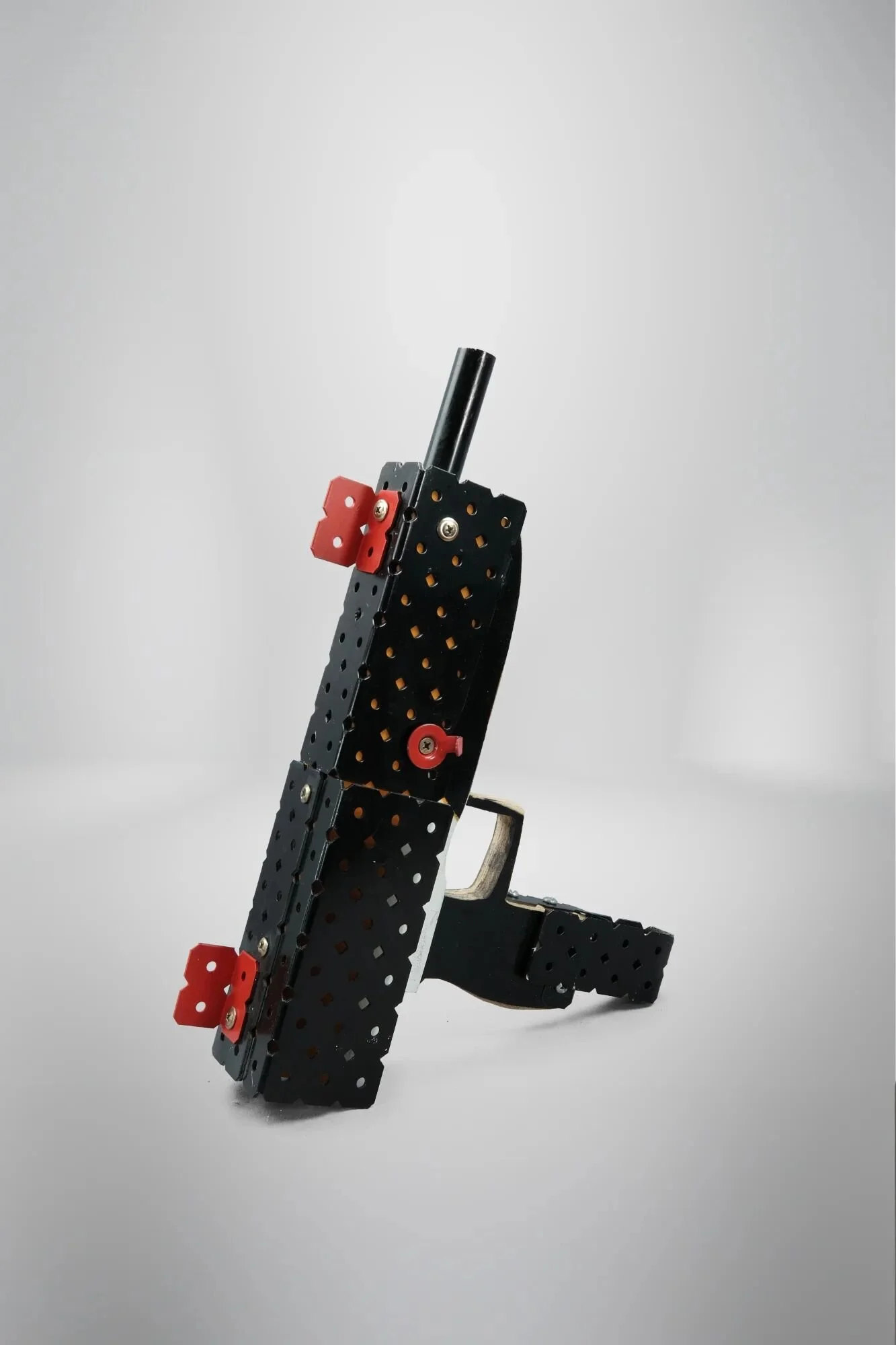 UZI form—guerrilla/asymmetric conflict weapon. Aluminium rod frame, plywood silhouette, L-bracket assembly. Trigger guard present. Trigger absent. Built for land struggles I cannot reach.