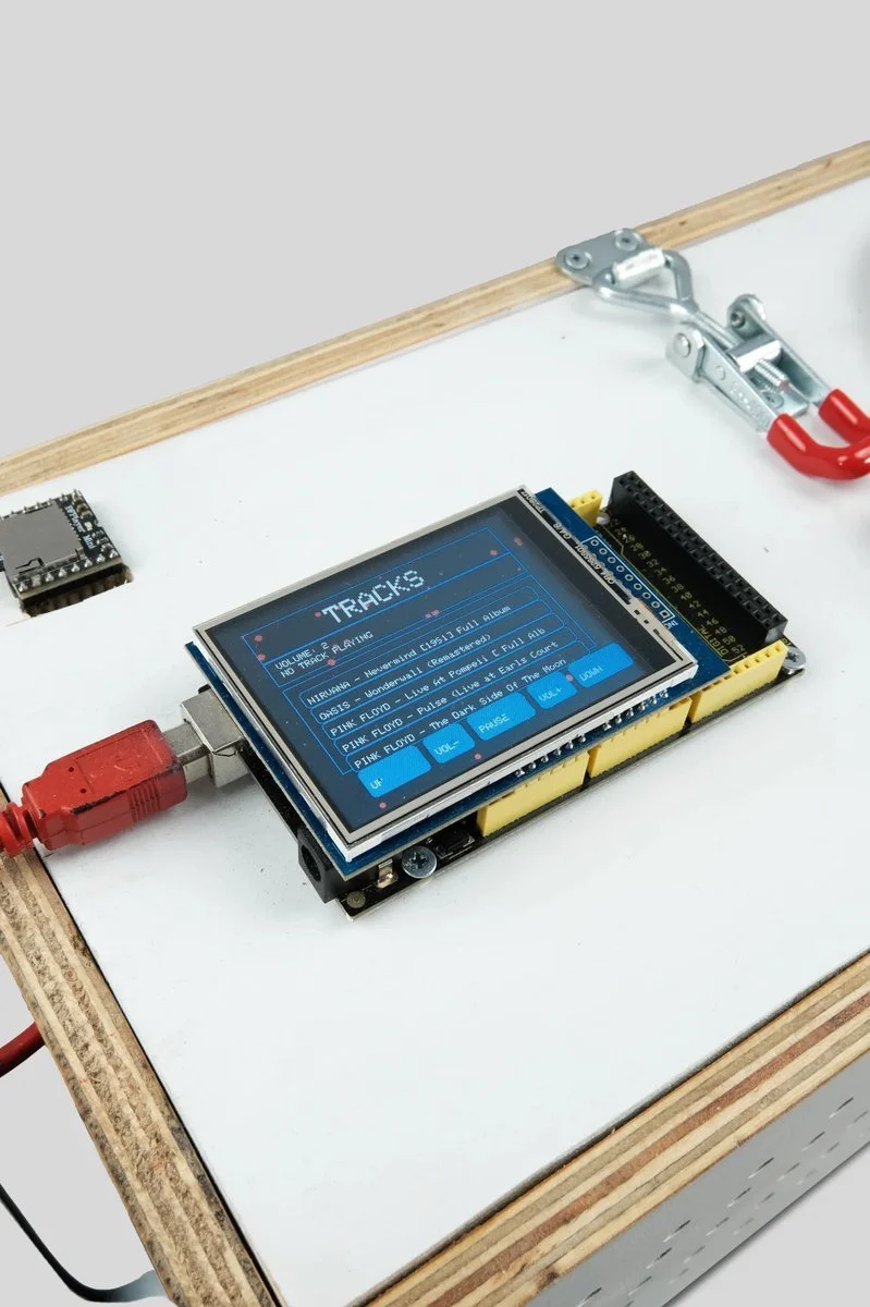 
Arduino Mega with shield drives display and controls. Salvaged plywood, visible construction, legible joinery. Pirated MP3s scrolling on screen—tribute built WITH the corruption it measures.