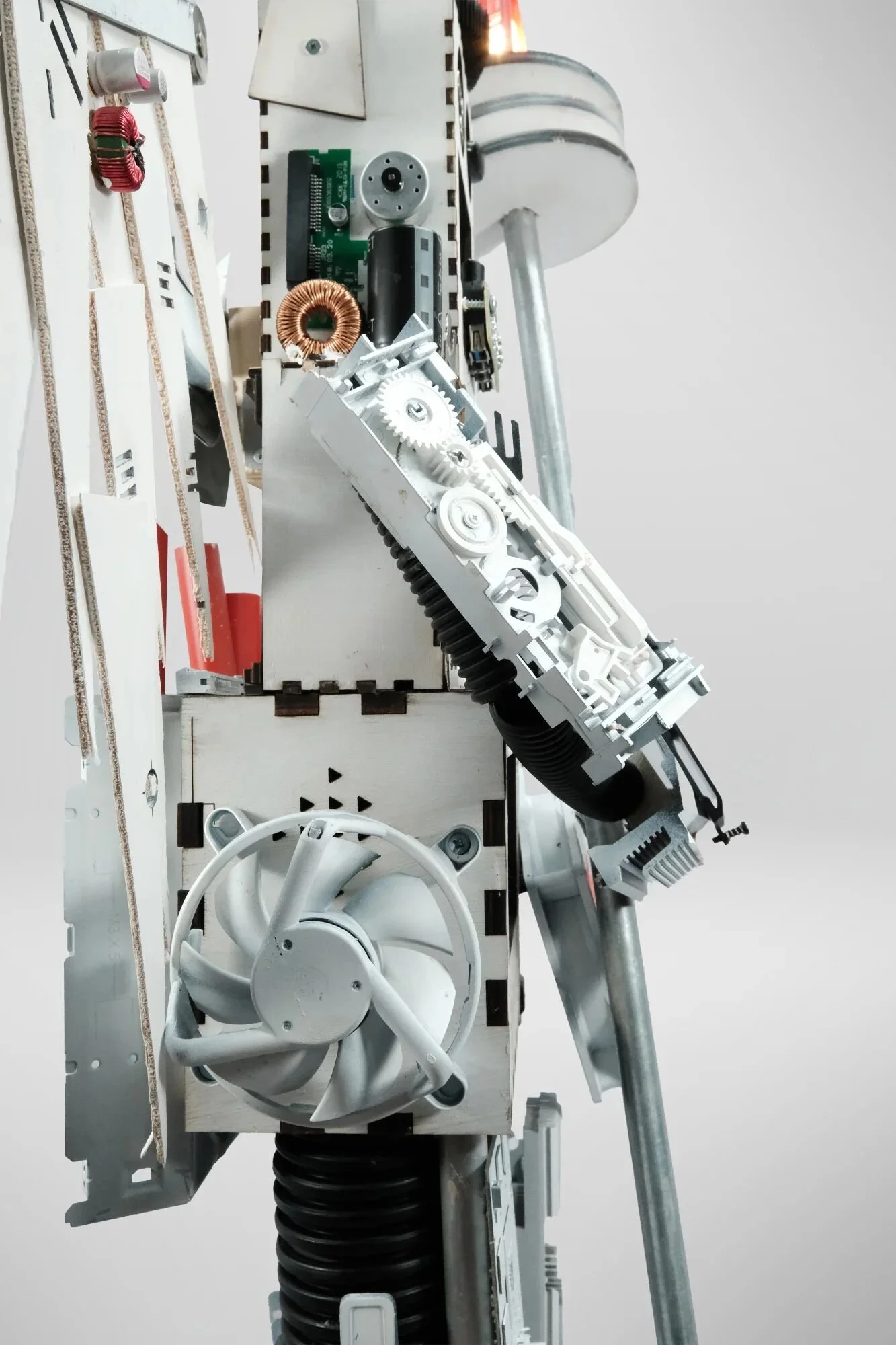 Torso detail: copper toroidal inductor, green circuit boards, computer cooling fan, visible wire looms. Incompatible systems from different eras—industrial electronics, consumer PC components, custom laser-cut frameworks—assembled through patient mat