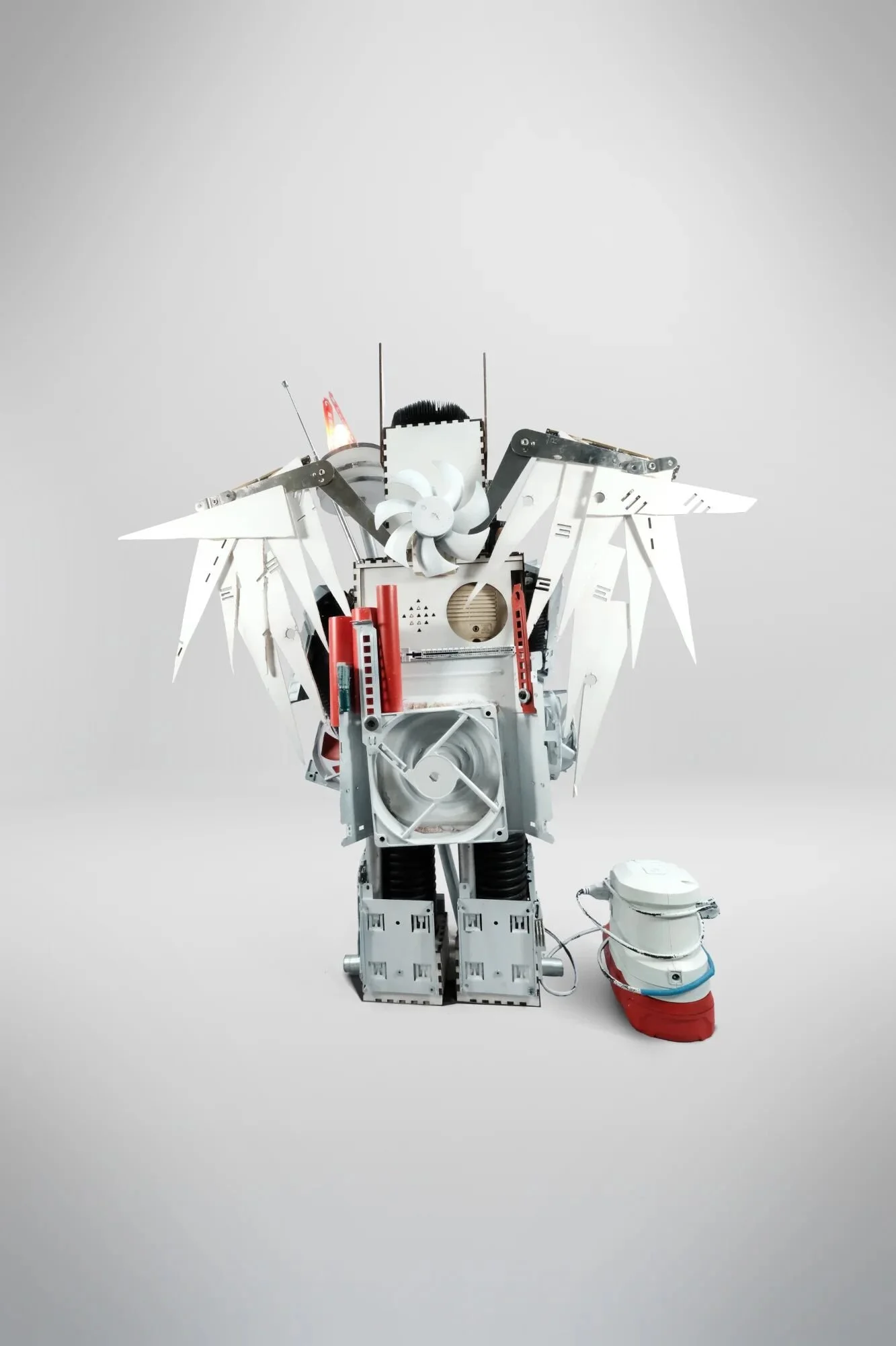 CPU heatsinks as ribcage, PCBs from multiple generations as skeleton. Laser-cut wooden feathers, steel staff with functional LED lamp. Incompatible systems assembled through custom framework showing how different technologies coexist without forced i