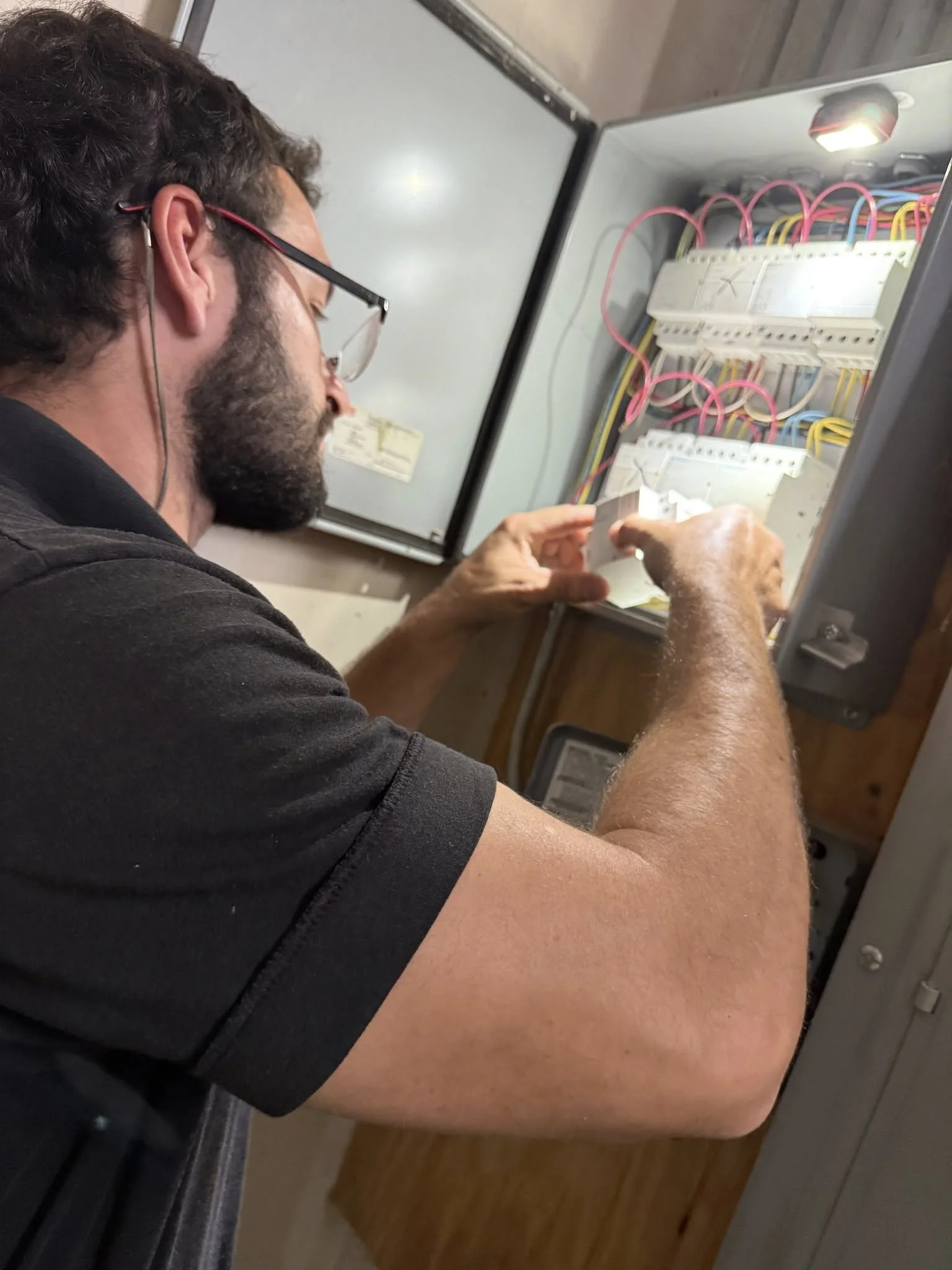 Big Ds Electric inspecting a panel for faults in a well lit corner.