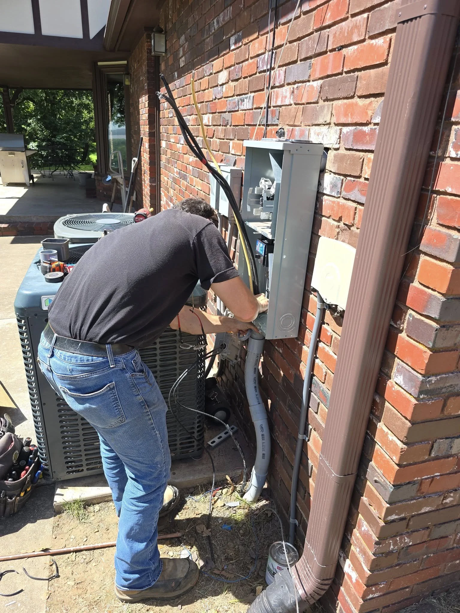 Man working from Big Ds Electric. Repairing a wiring issue on an outdoor panel by the HVAC system on a brick wall.