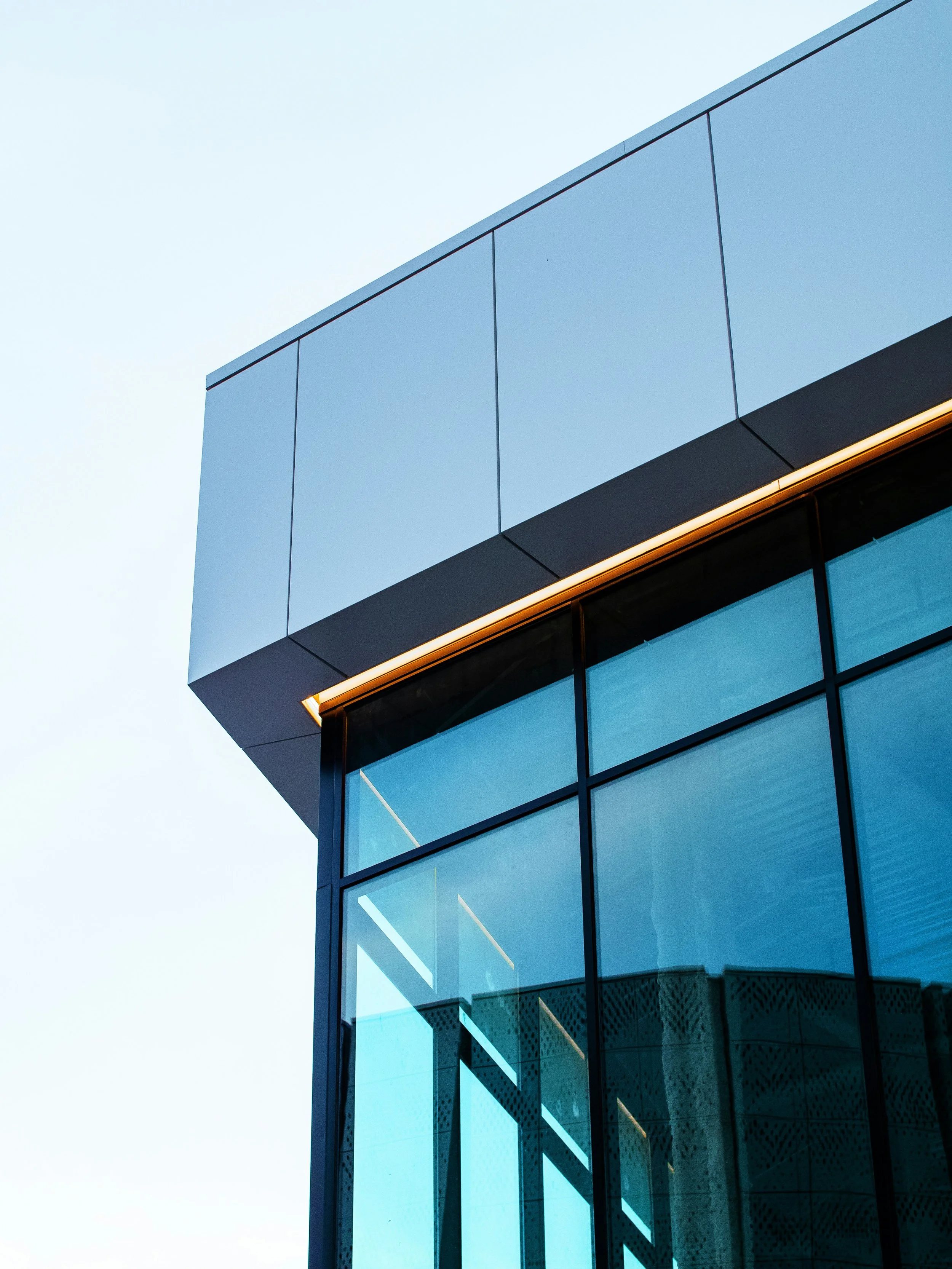 Close-up of a modern glass building with reflective blue windows and orange lighting accents, angled against a clear sky.