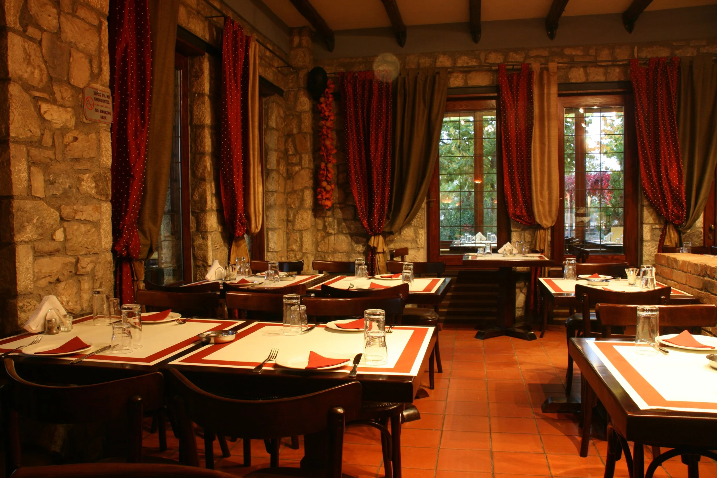 Εσωτερικός χώρος στο Φαγοτόπι με πέτρινους τοίχους, μεγάλες κουρτίνες και τραπέζια στρωμένα με σερβίτσια. Ζεστή ατμόσφαιρα φιλοξενίας στη Λίμνη Πλαστήρα.