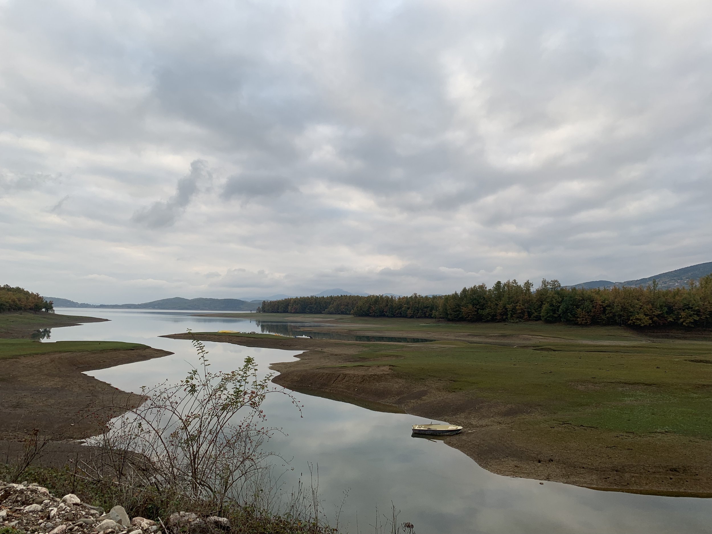 Μικρή βάρκα στις όχθες και φόντο τους λόφους της Λίμνης Πλαστήρα. Τοπίο που αποτυπώνει τη γαλήνη της θεσσαλικής φύσης.