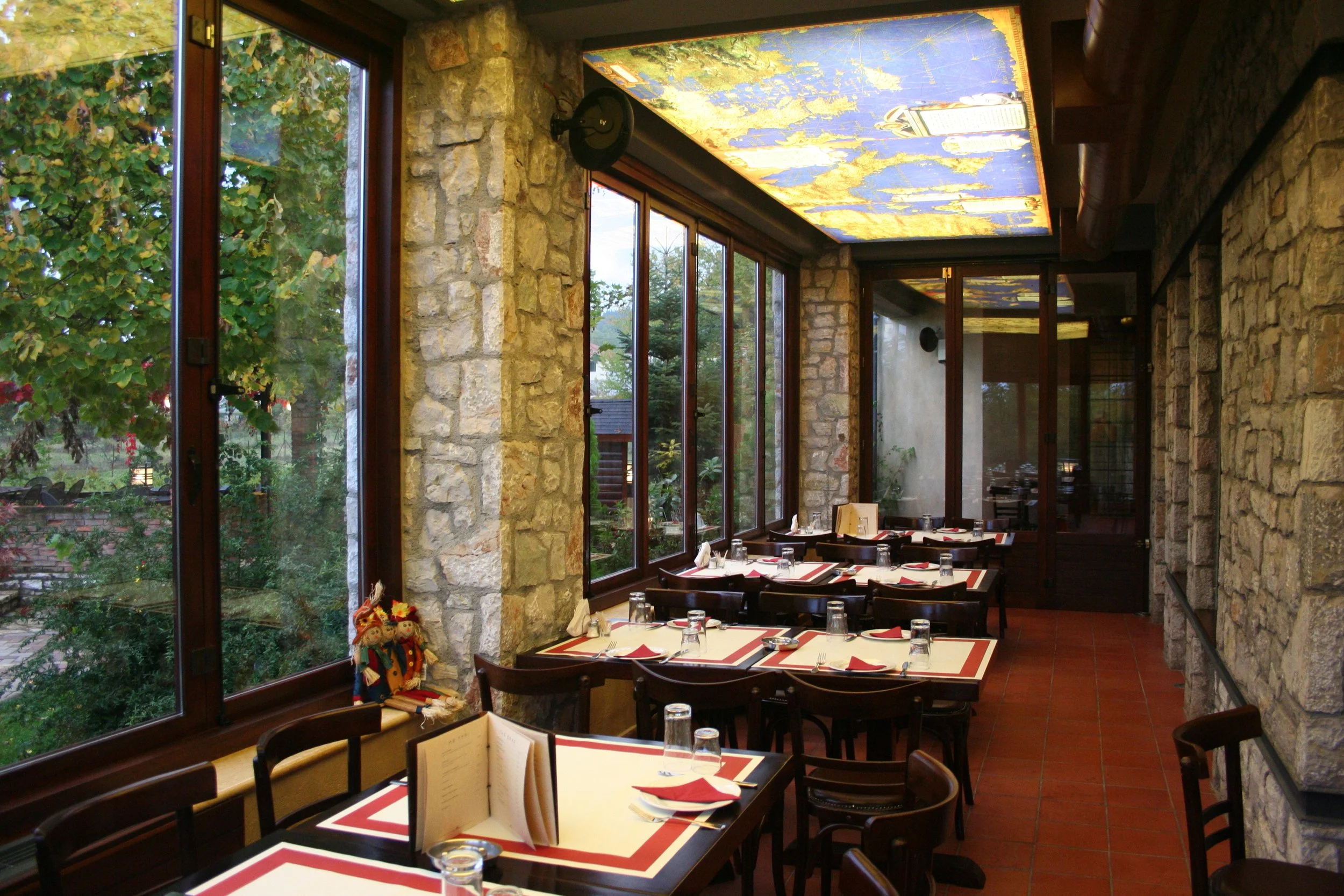 Εσωτερικός χώρος στο Φαγοτόπι με πέτρινους τοίχους, ξύλινα τραπέζια και διακοσμητική οροφή με χάρτη. Ζεστή ατμόσφαιρα δίπλα στη Λίμνη Πλαστήρα.
