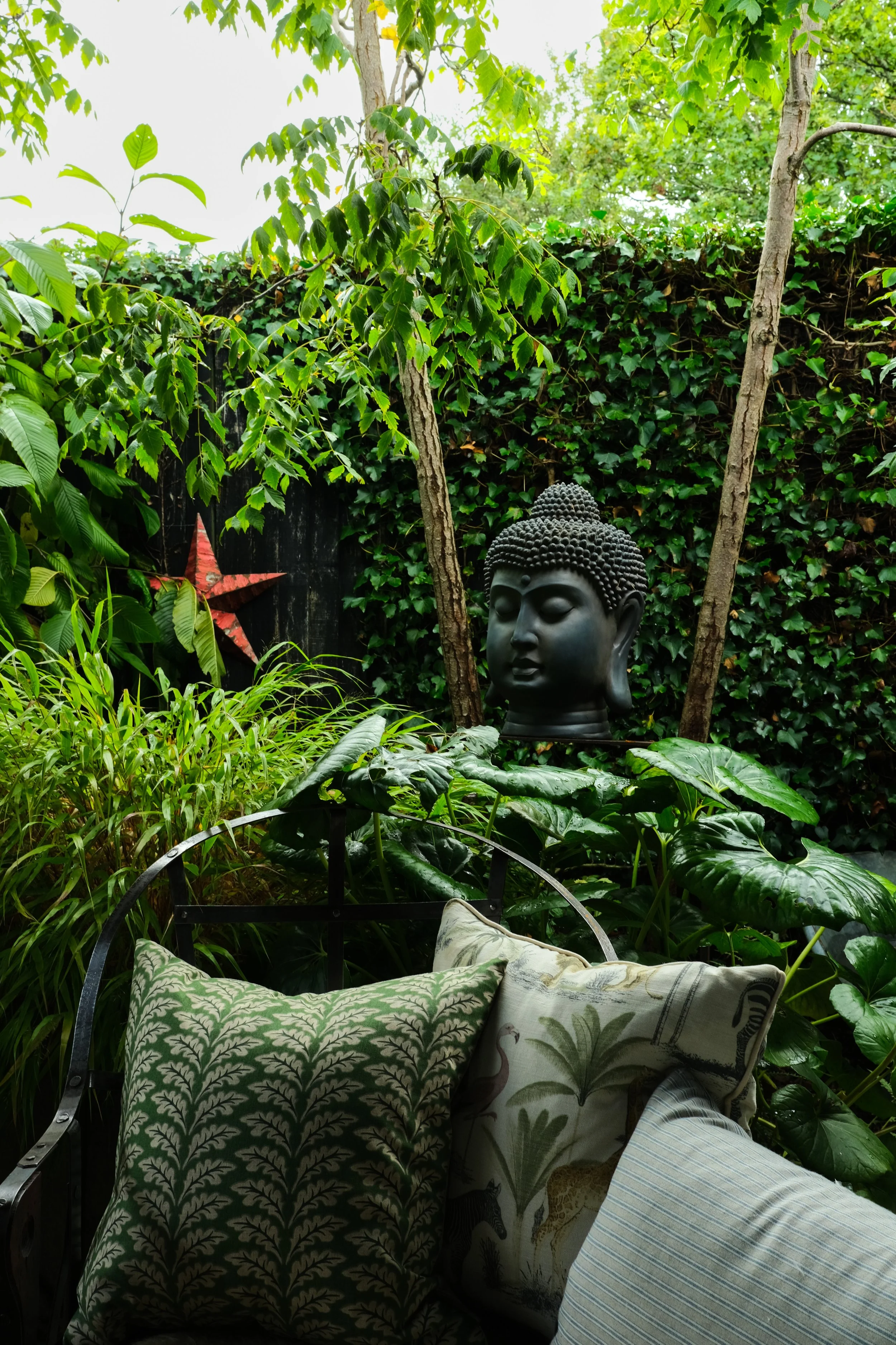 A garden sofa full of cushions surrounded by plants