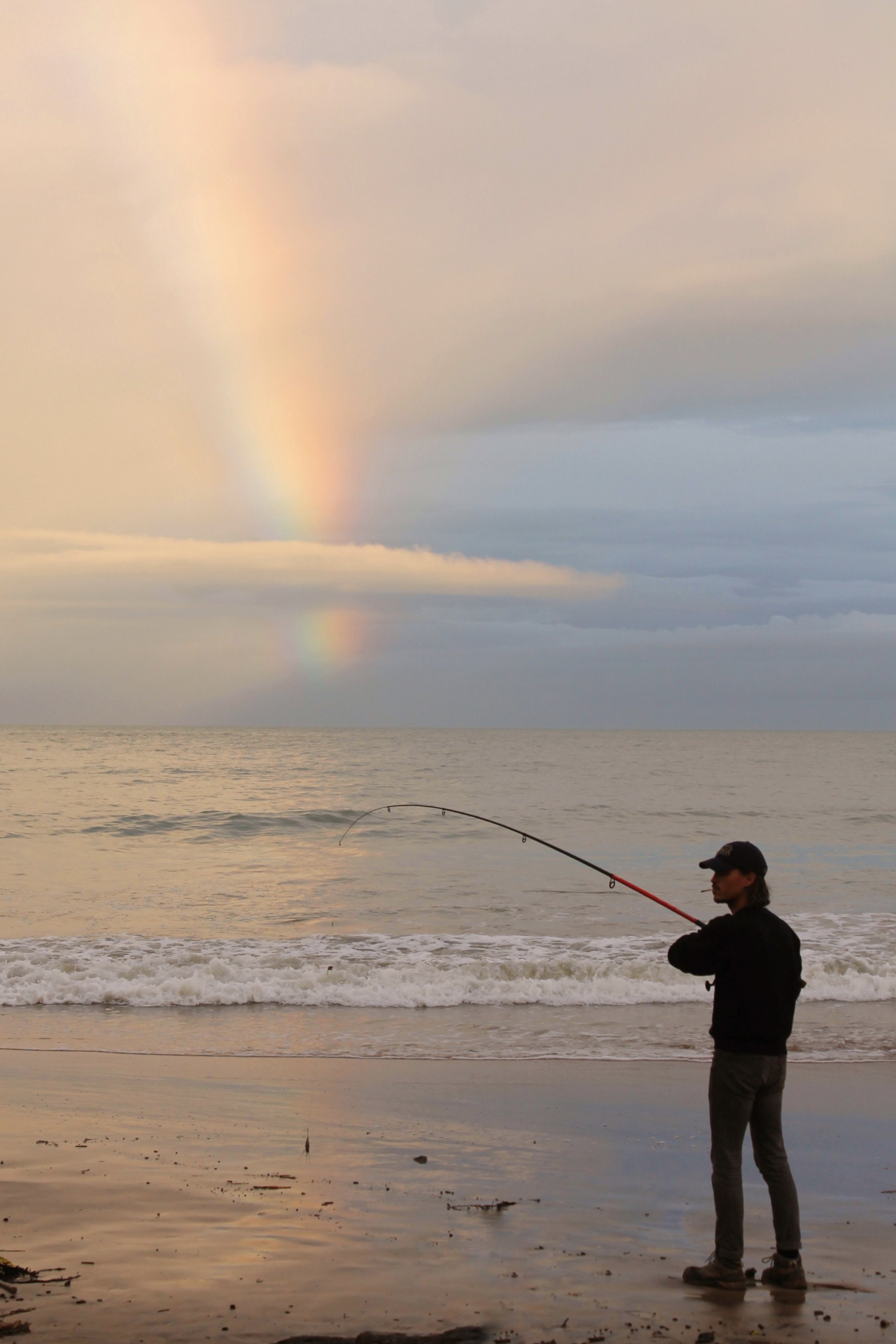 Fisherman at low tide with a pink and soft rainbow in the sky