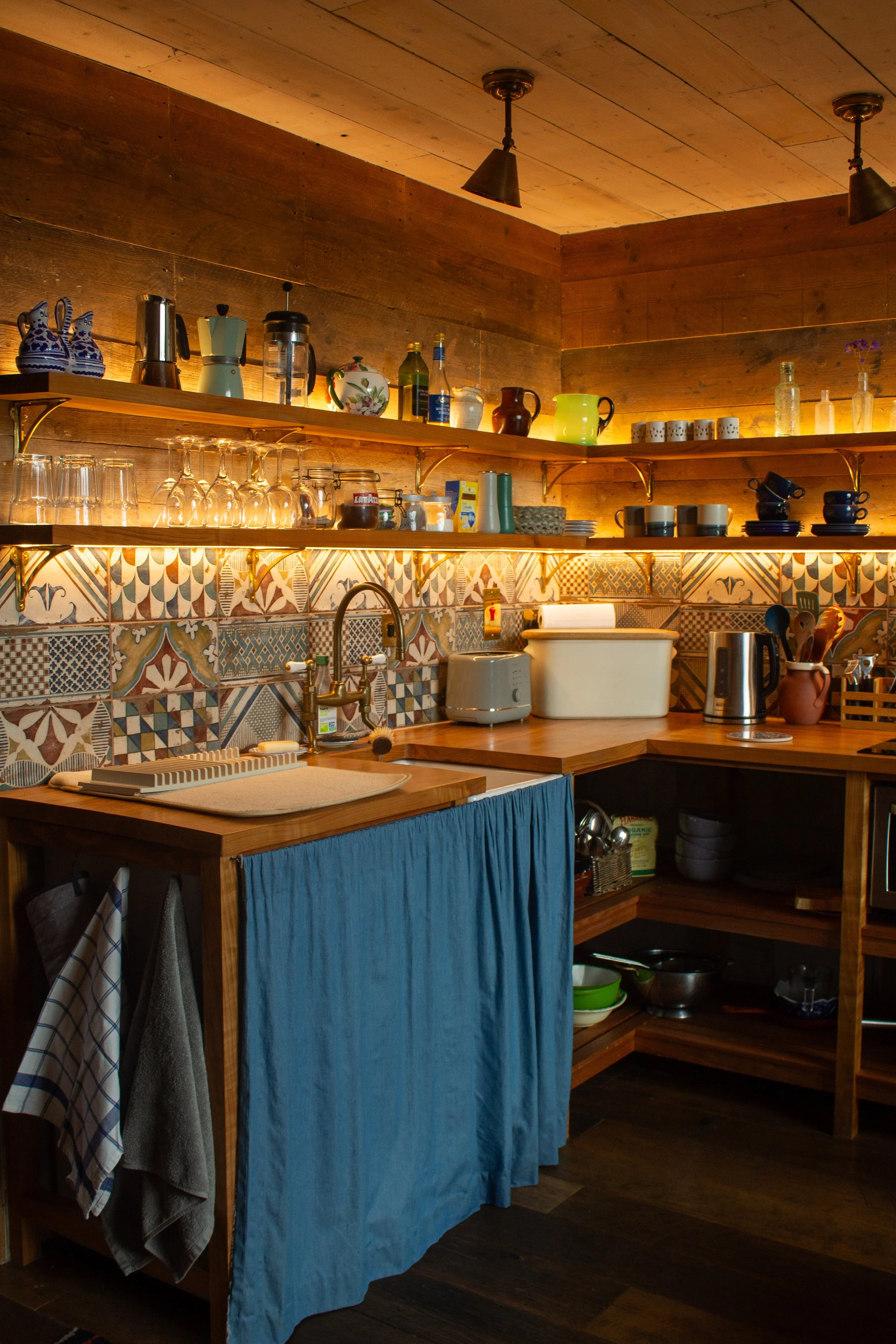 A cabin kitchen with warm lighting, blue cupboards and colourful pattern tiles