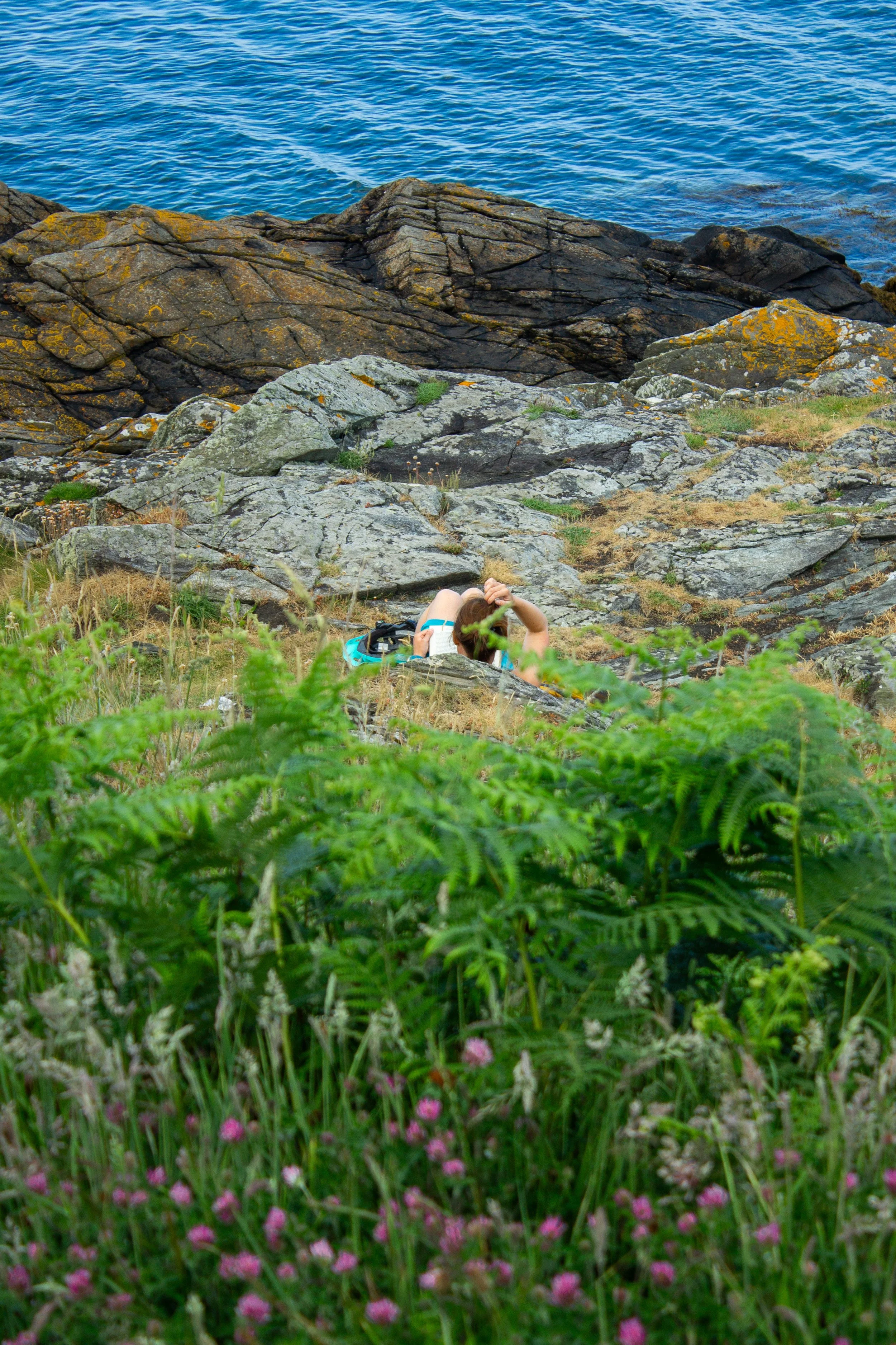 A lady lying down and reading a book along a coastal path on the Isle of Man