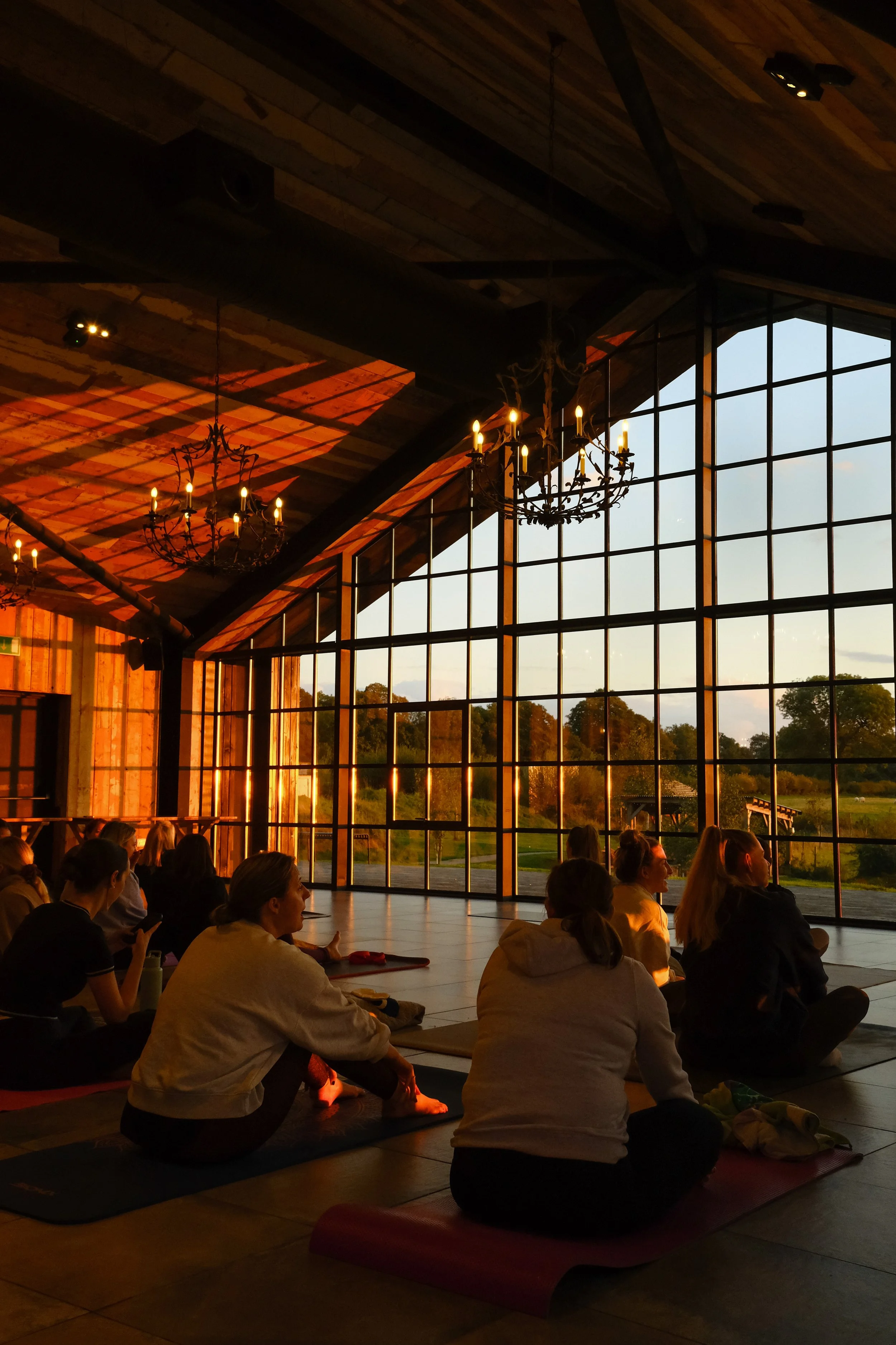 An orange sunset shining into a pilates class in a barn with huge windows and rustic style