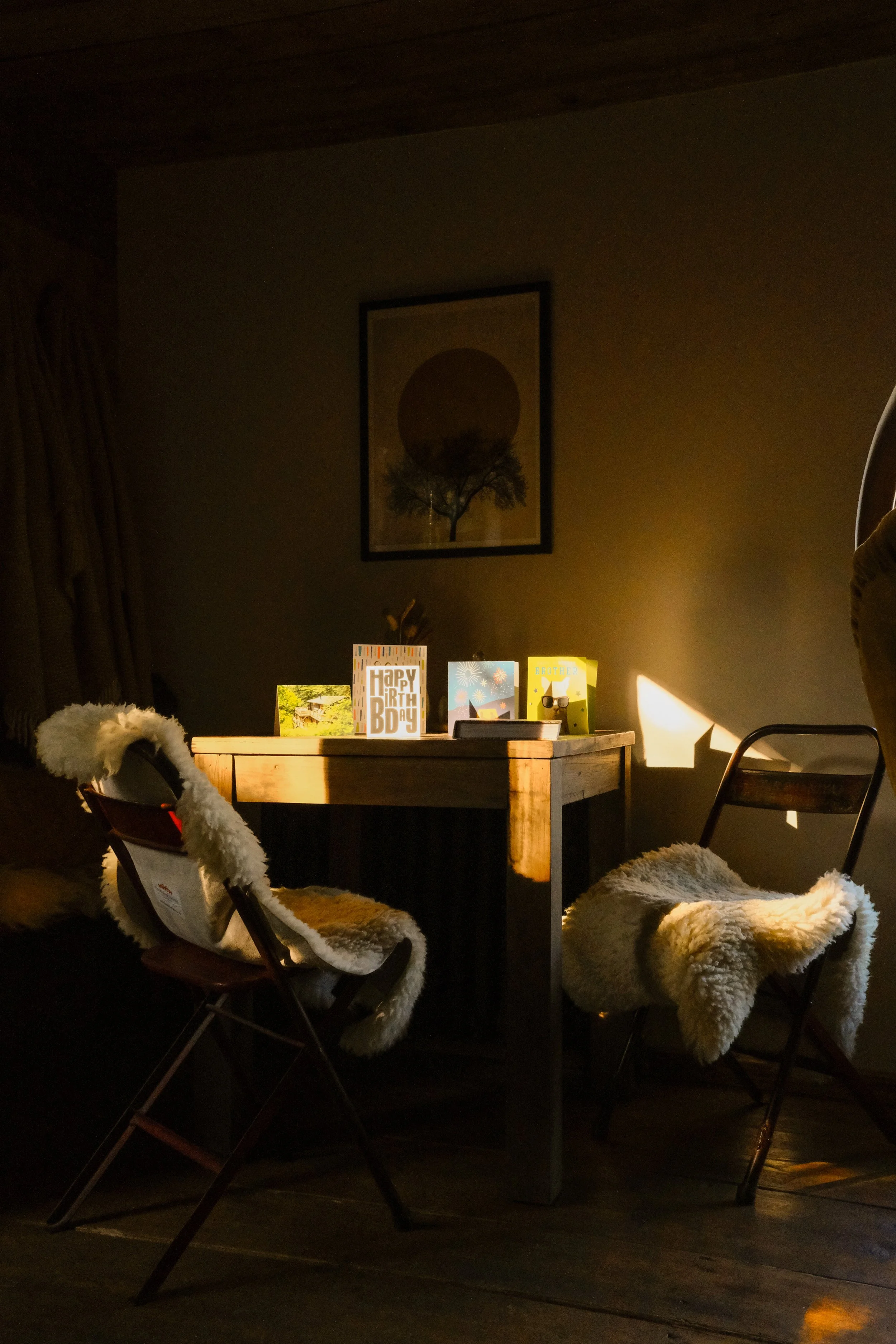 A cabin dinner table with sheepskin throws over the chairs and sunset reflections on the wall