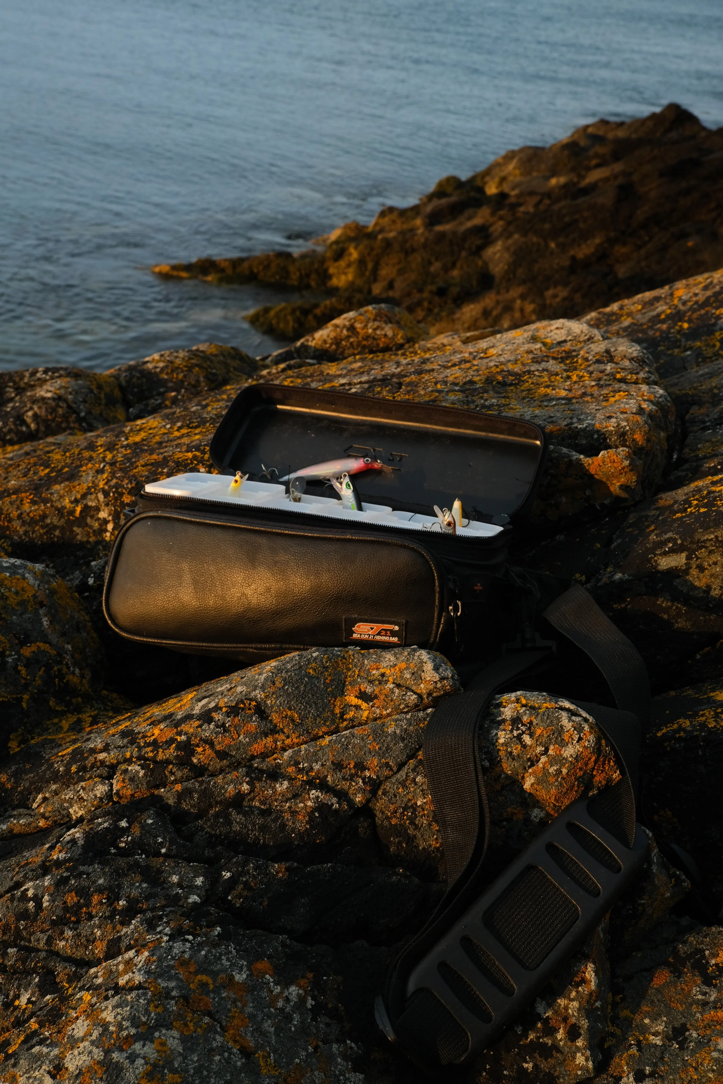Fishing gear in a fishing bag on the rocks at sea during sunset