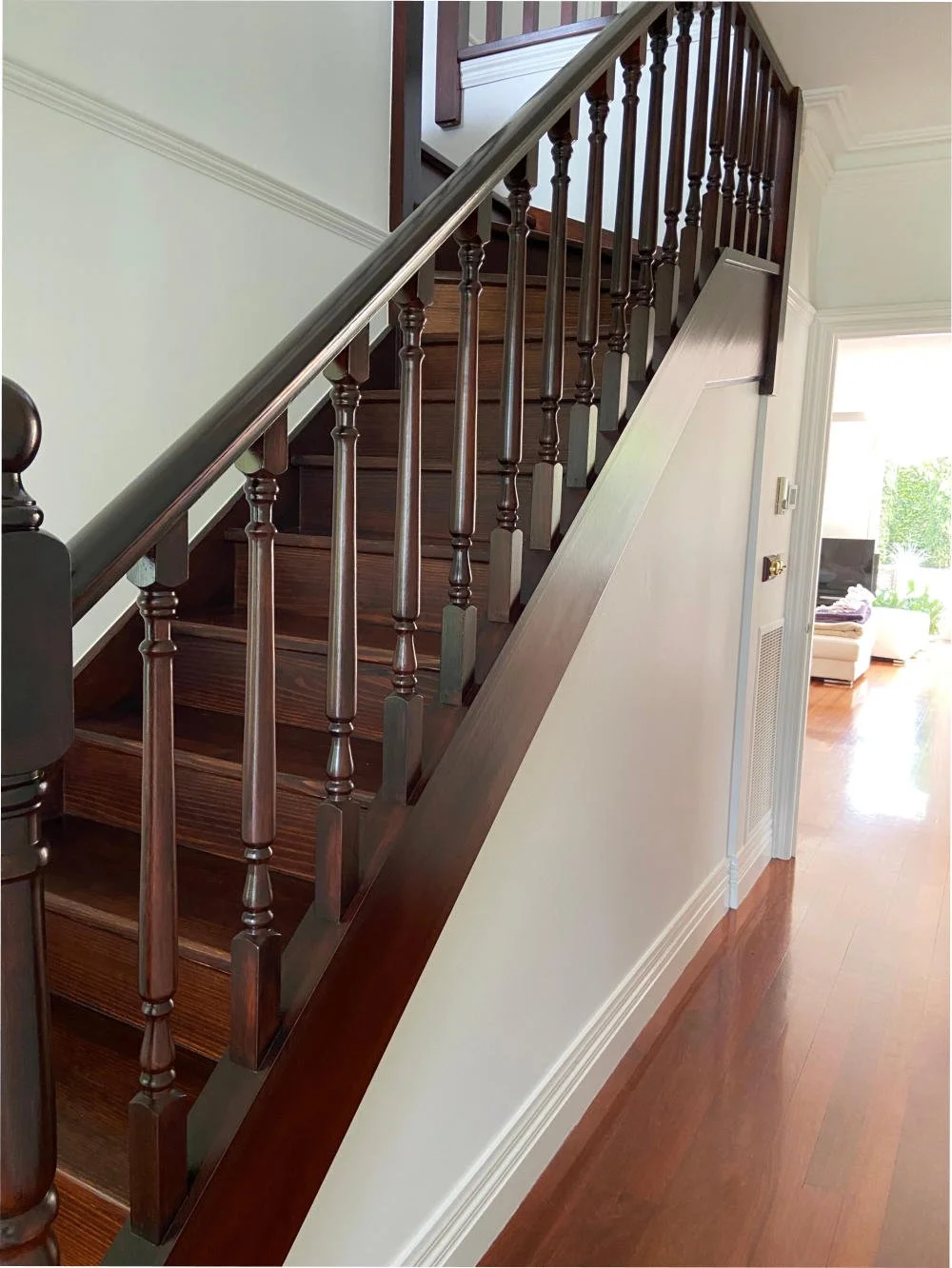 Interior view of a staircase with wooden steps and dark wood handrail, leading to an upper floor in a house with white walls and hardwood flooring.