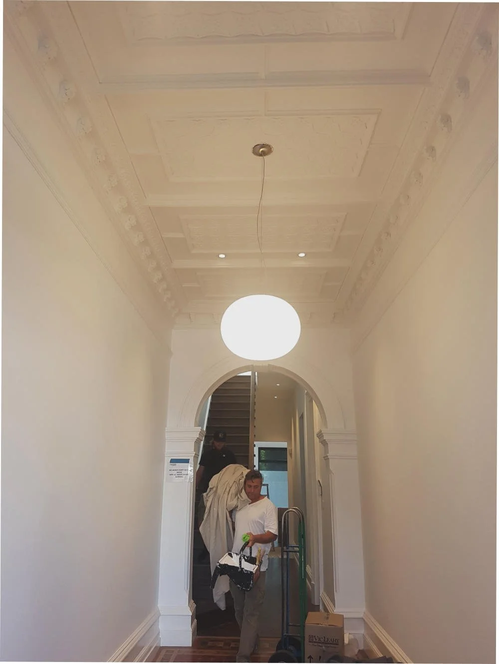 Interior hallway with ornate ceiling, white walls, and archway entrance. 