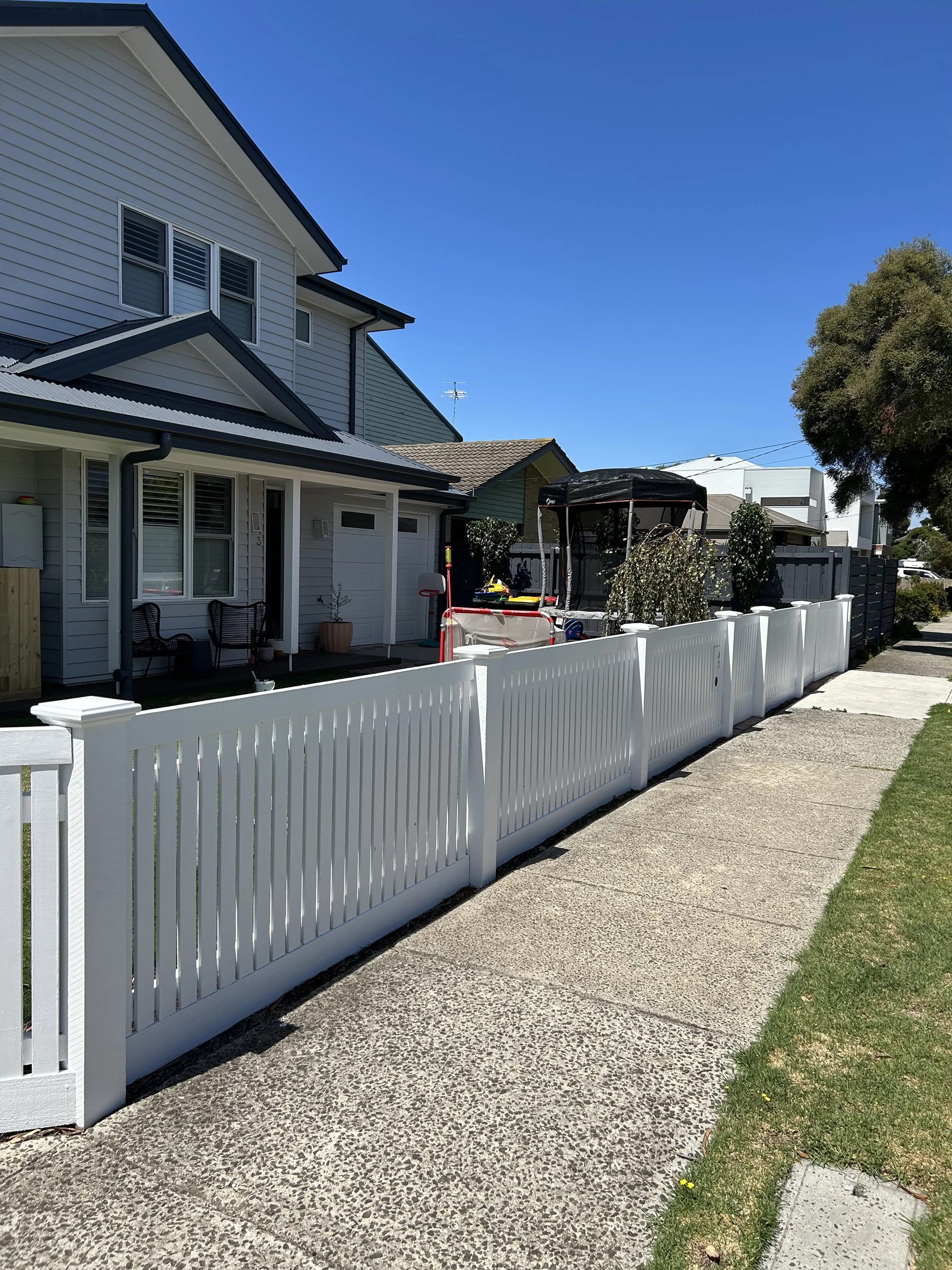 Front yard with a white picket fence, sidewalk, and house in the background. 