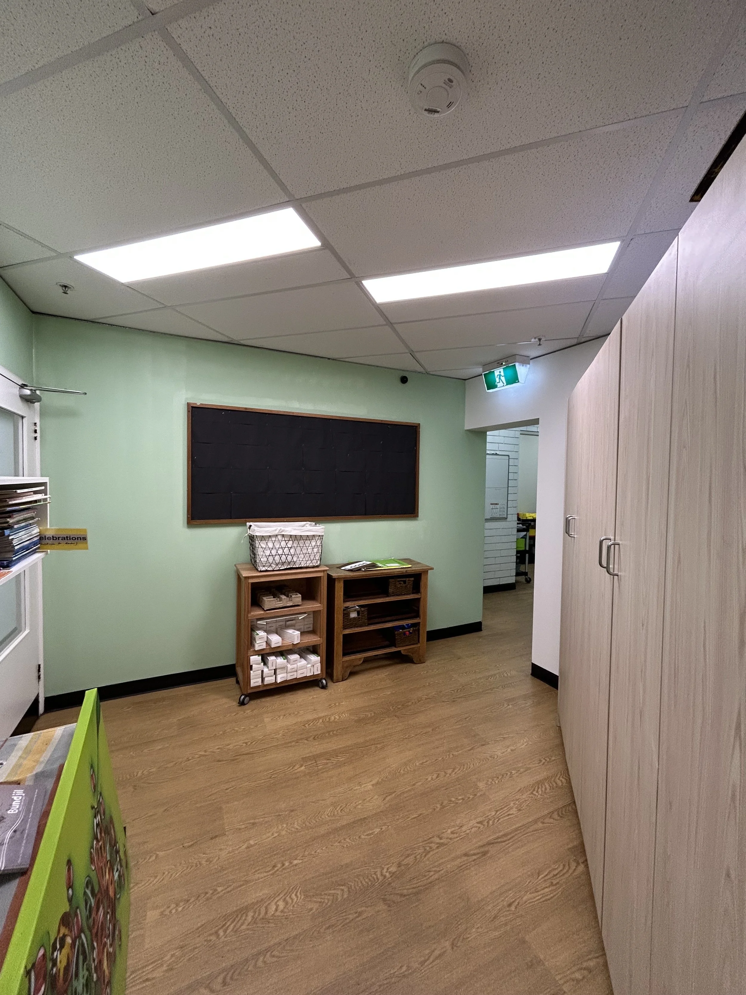 Interior of a room with light green walls, wooden floor, and a white ceiling with fluorescent lights. 