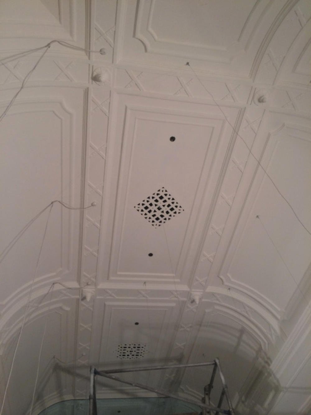 Ceiling with decorative molding, vents, and wires hanging, with scaffolding at the bottom.