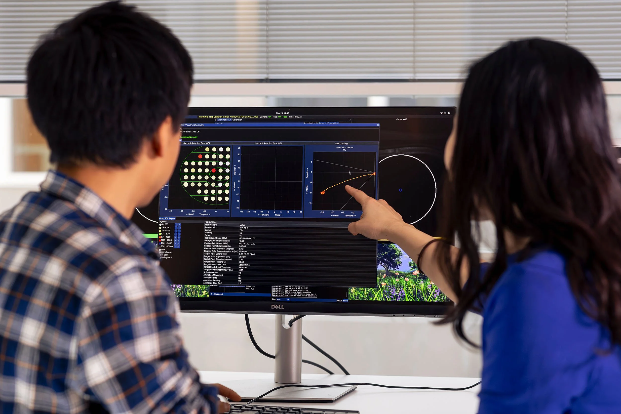 Two researchers looking at results in medical software, a large monitor screen displaying test results, near a window.