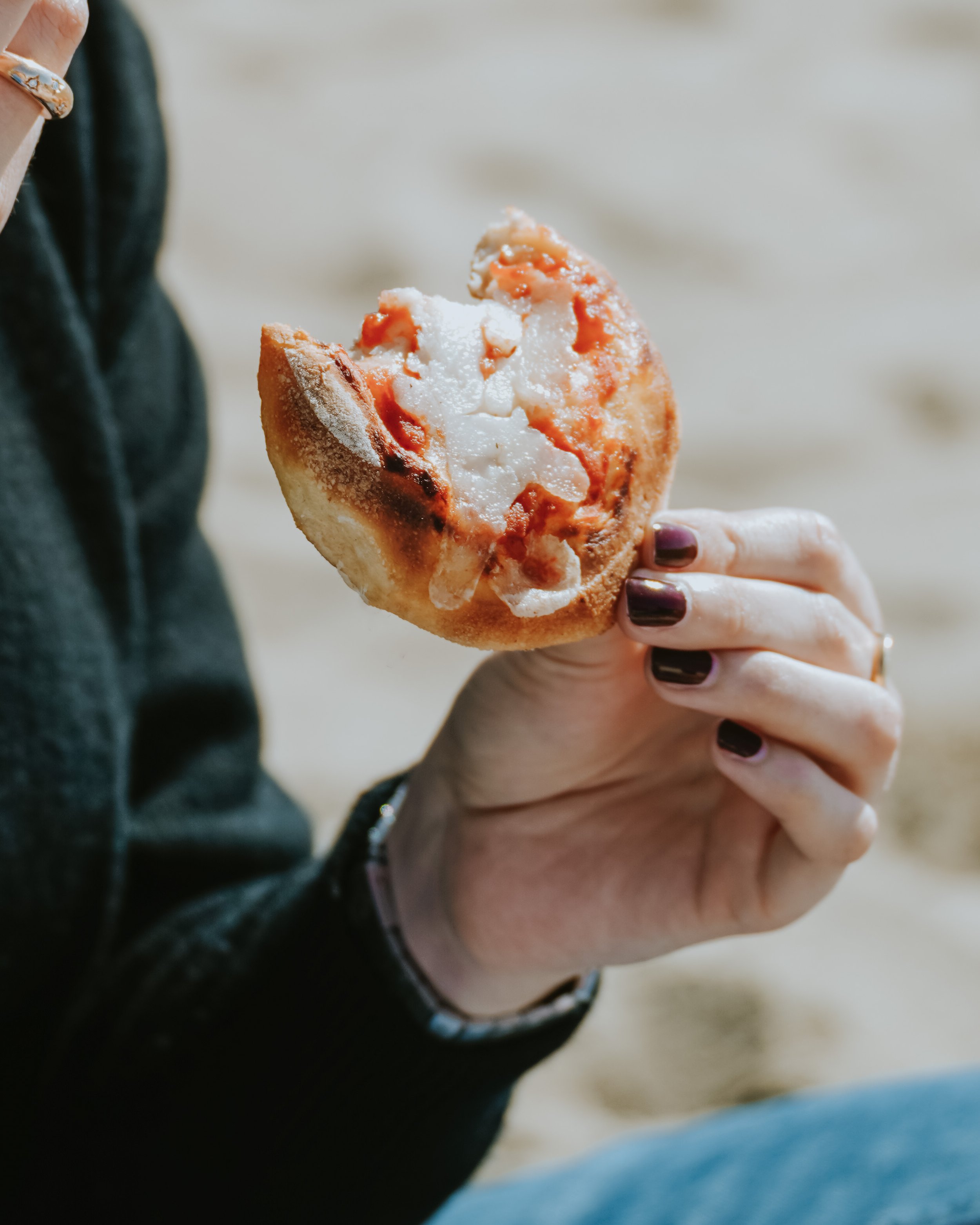Persona che tiene in mano una pizza con formaggio e pomodoro. Sfondo di spiaggia o sabbia. Pizzeria Alfiero Marina di Massa.