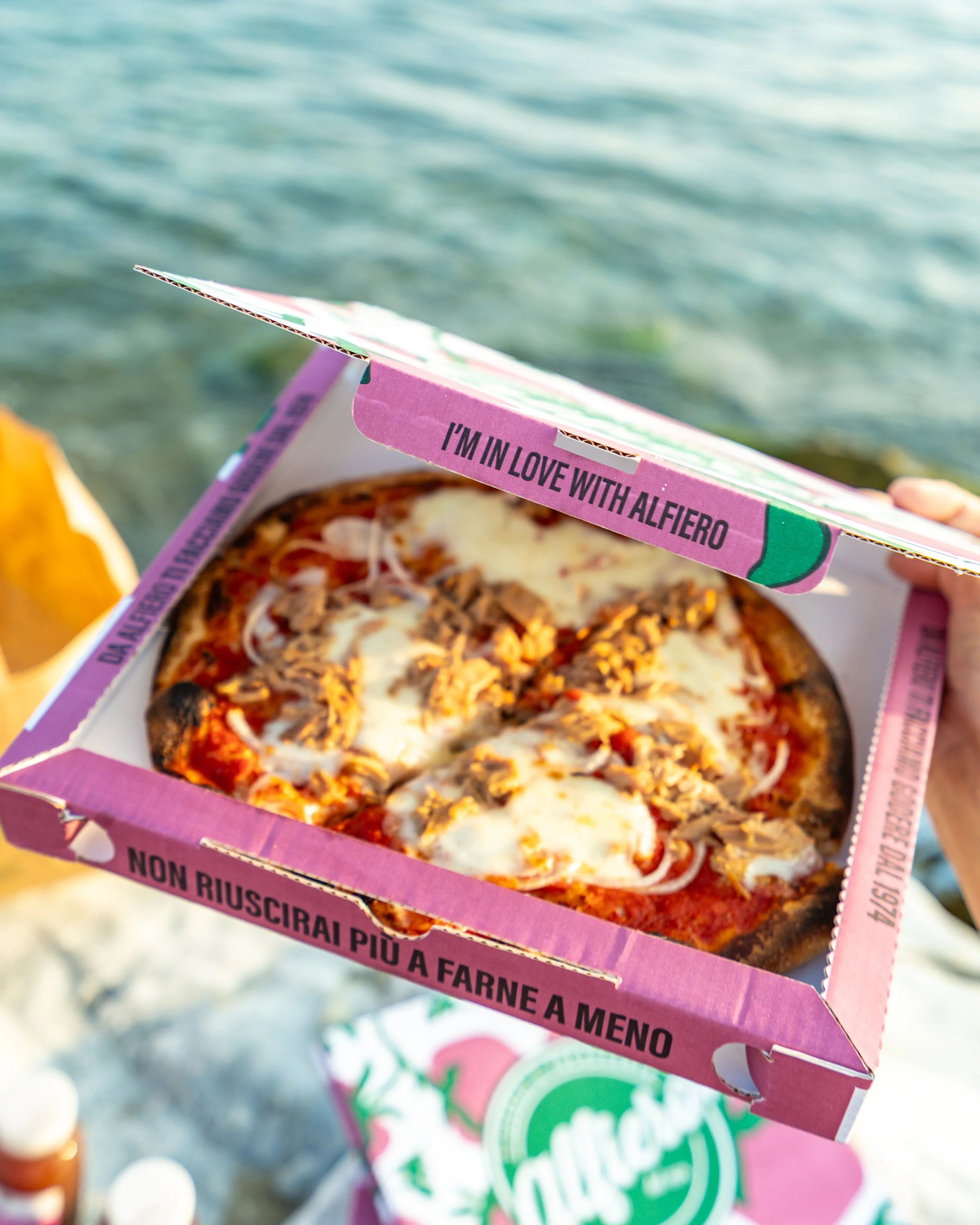 Una scatola di pizza con formaggi e tonno., tenuta sopra una superficie vicino all'acqua.Pizzeria Alfiero Orto di Alfiero Marina di Massa.