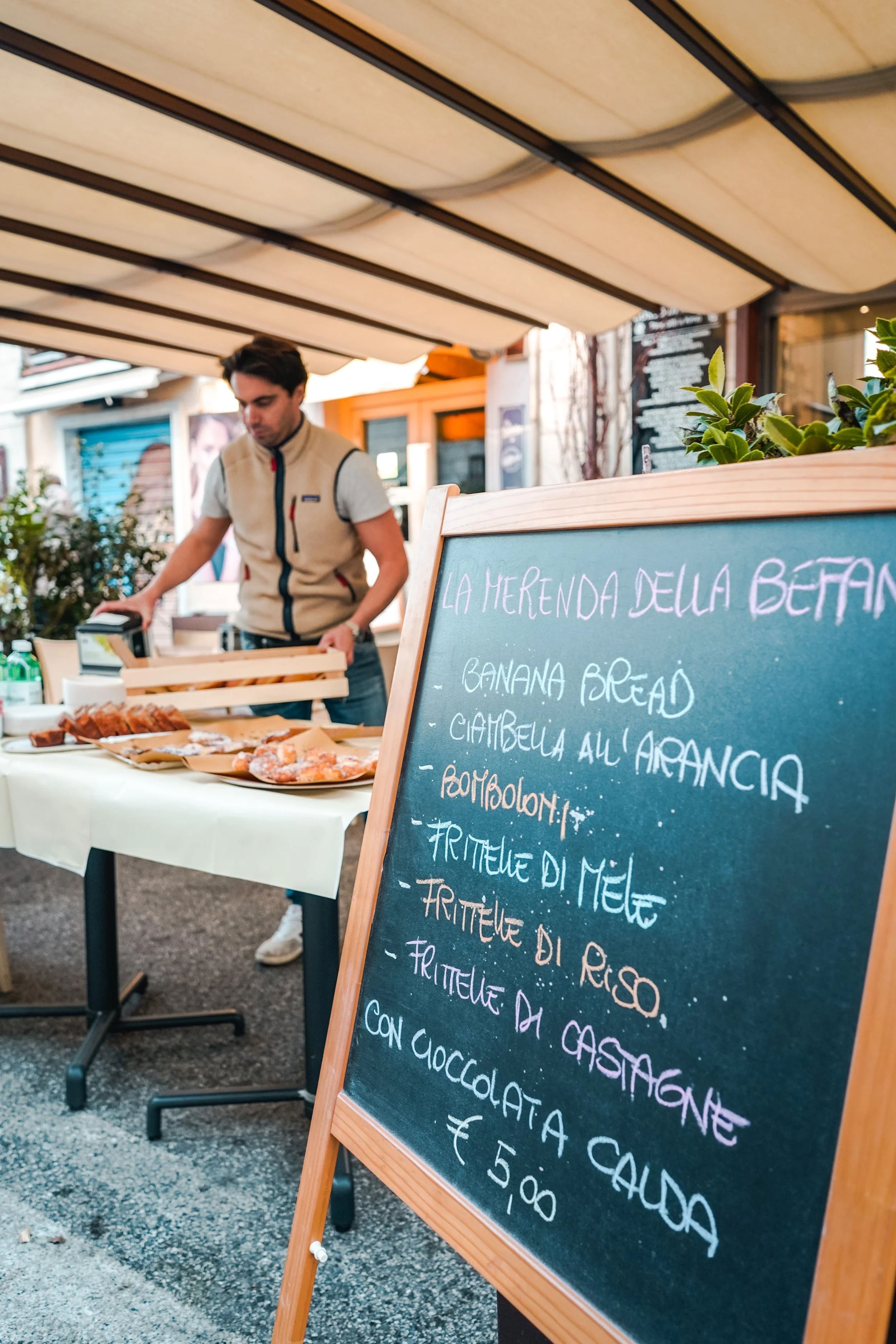 Lista di snack e merende disponibili in un lavagna all'aperto: banana bread, arance con camomilla, crepes, varie Creme, con prezzo di 5,80 euro. Pizzeria Alfiero Orto di Alfiero Marina di Massa.