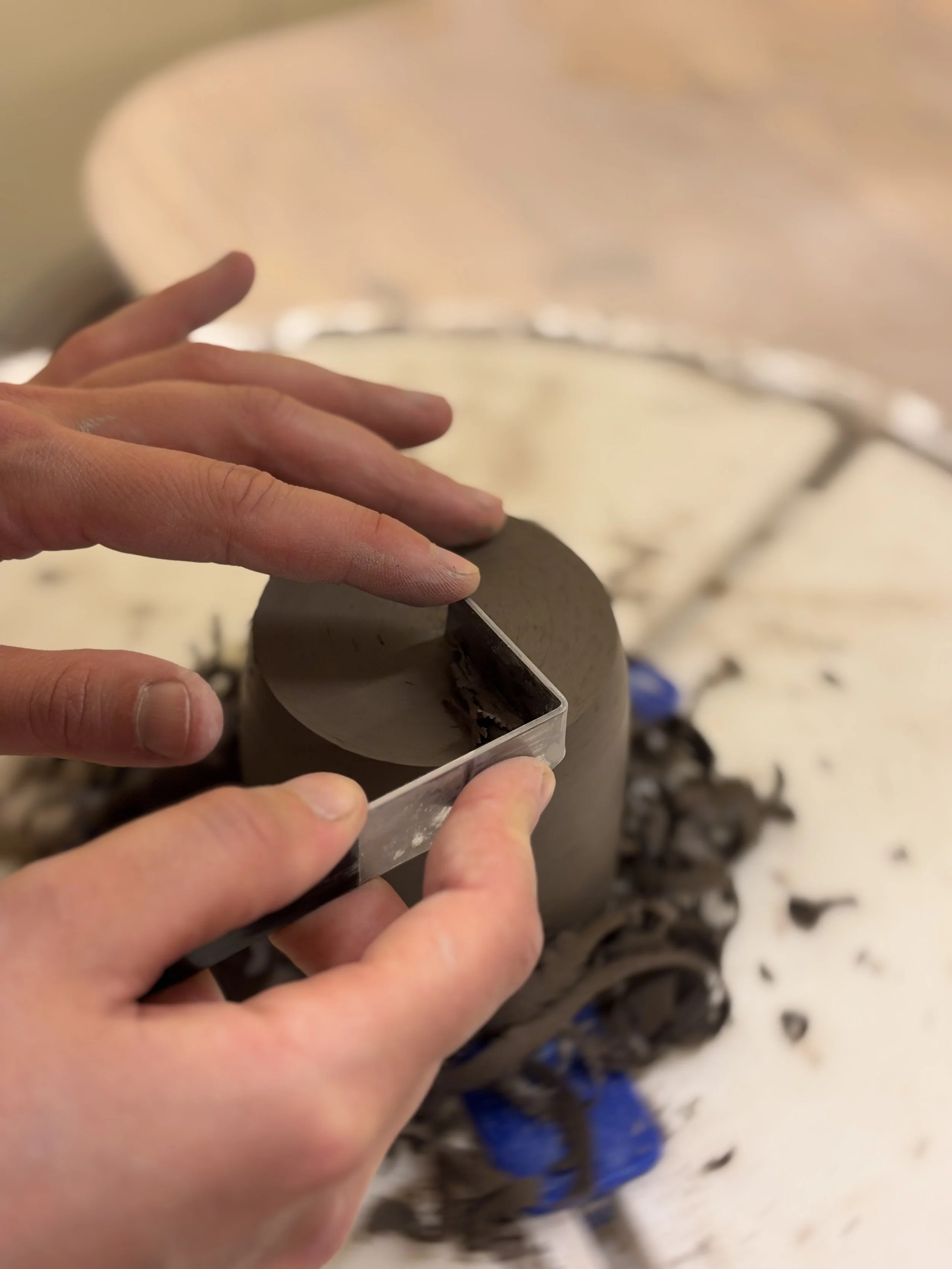 En person former en svart keramikkrukke med en mal for å lage jevn fasade.