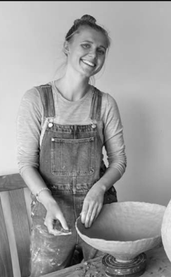 Kvinne lerende i et verksted med keramikk, holder en keramisk skål.