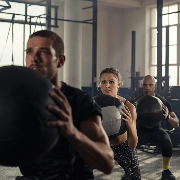 Tres personas haciendo ejercicio con pesas en una clase de circuitos en un gimnasio.