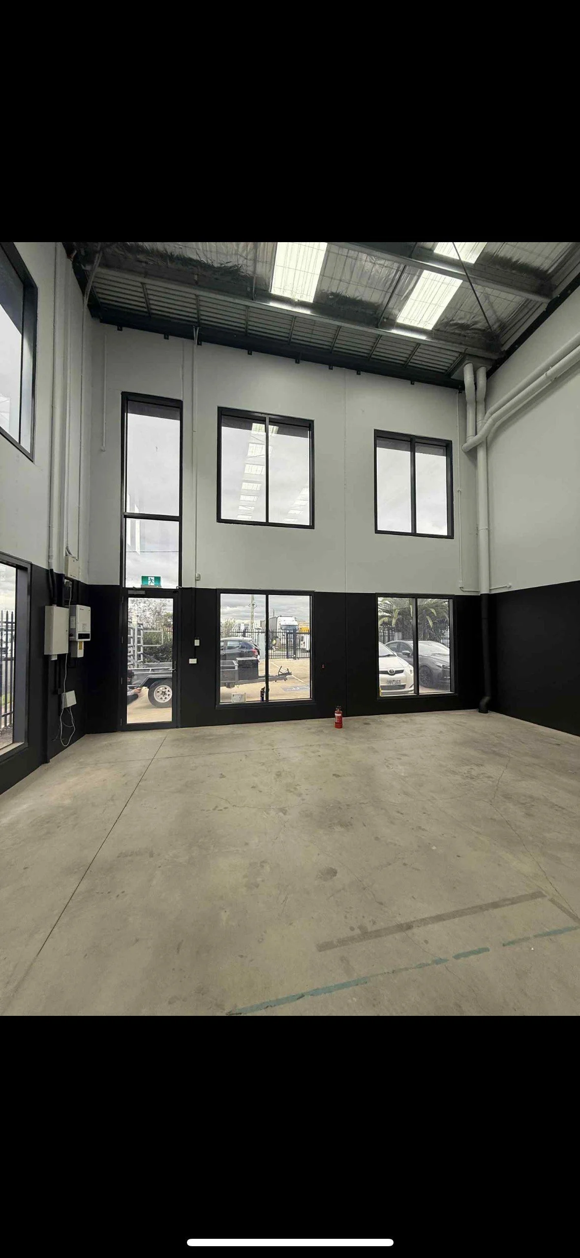 Empty commercial or industrial interior with large windows, concrete floor, and high ceiling with skylights.