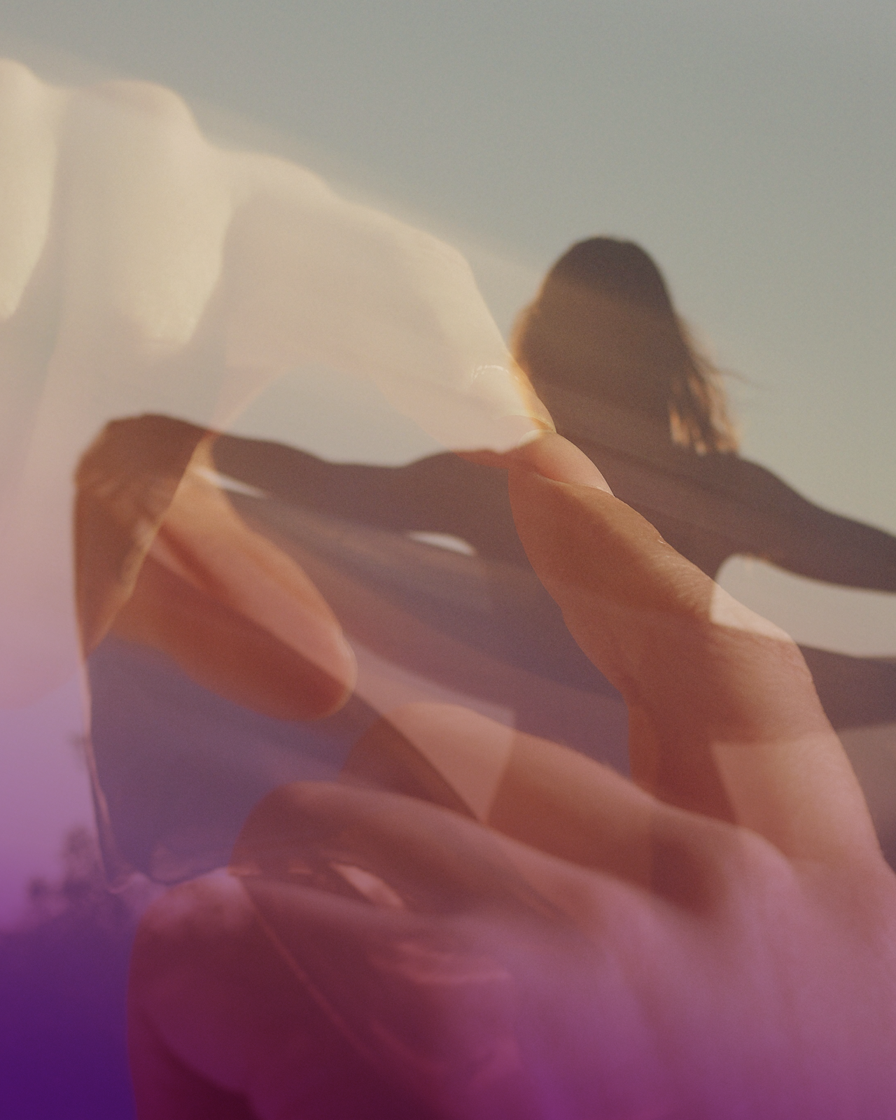 A person with long hair lying on the beach, with an artistic overlay of hands and toes, creating a layered, abstract effect, during sunset or sunrise.