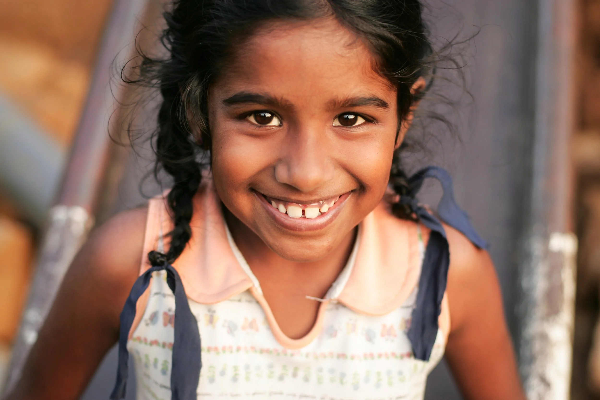 Portrait d'une jeune fille Sri Lankaise. C'est un gros plan. Elle a les yeux marrons, sourit à pleines dents et regarde droit dans l'objectif