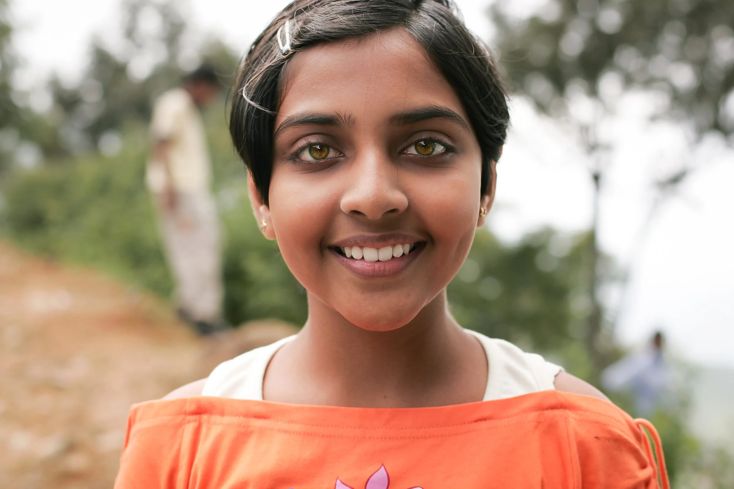 Portrait d'une jeune fille Sri Lankaise. Gros plan.  Elle a les yeux verts marrons clairs, un magnifique visage. Elle a les cheveux courts et sourit. Ses dents sont parfaitement blanches. C'est un gros plan. 