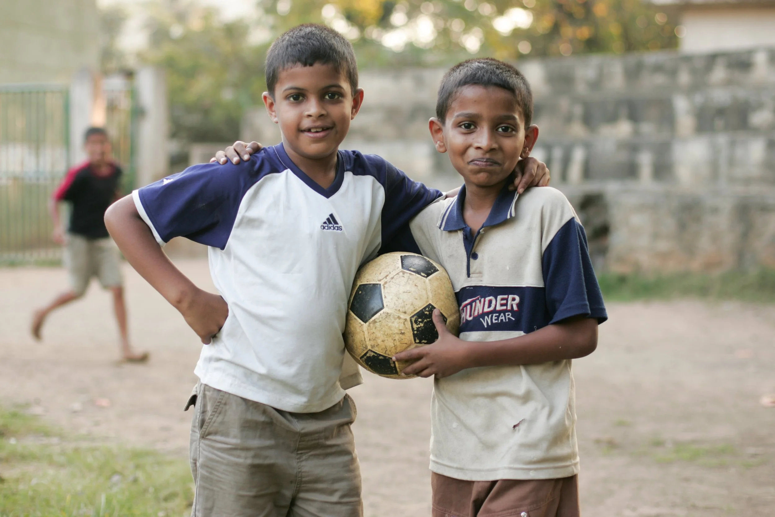 Portrait de deux garçons Sri Lankais sur une aire de jeux à l'extérieur, au Sri Lanka. Ils se tiennent par l'épaule et tiennent un ballon de football entre eux. 