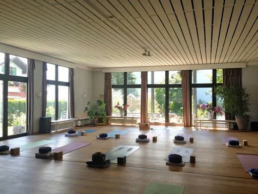 Großer heller Yoga Raum mit vielen Fenstern und Sicht auf Natur, Bäume und Berge, viele Yoga Matten, Sitzkissen und Yoga Klötze auf Holzboden für Kundalini Yoga Retreat, Wochenende und Auszeit in Natur unter Frauen