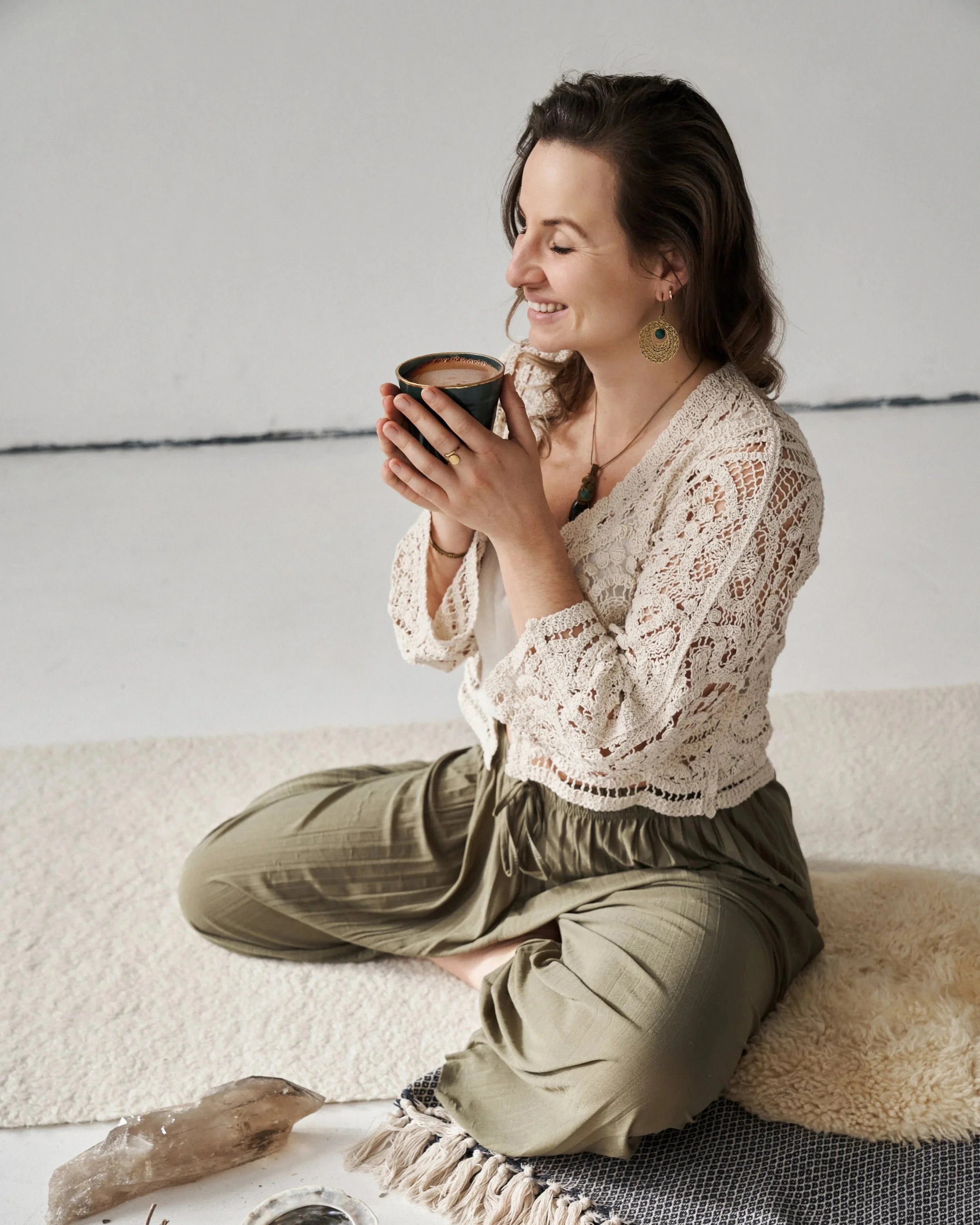 Franziska Riedl, Yoga Lehrerin, sitzt im Schneidersitz auf einem Teppich und hält in einer Zeremonie eine Tasse Kakao, der Heilsam und Herzöffnend ist in der Hand für Selbstliebe, Verbundenheit und weibliche Intuition