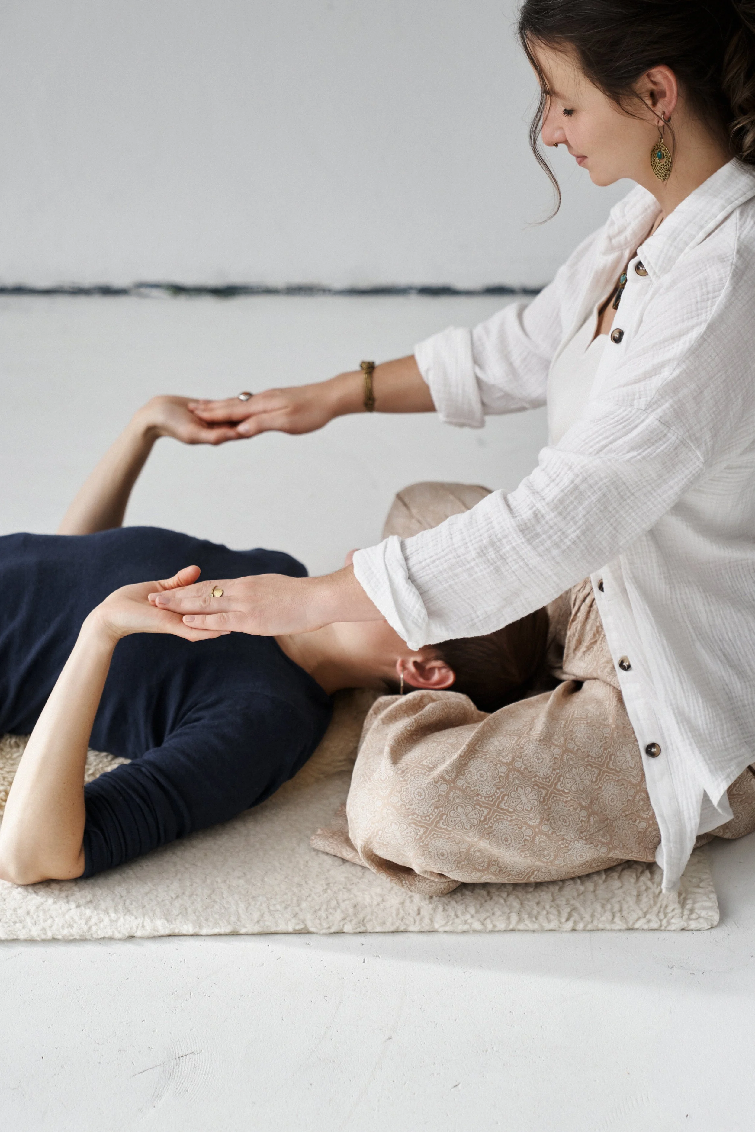 Franziska Riedl sitzt im Schneidersitz und trägt ein weißes Hemd und hält die Hände einer Frau, die am Boden vor ihr liegt um eine Energiebehandlung zu geben und Blockaden und Spannungen zu lösen für geistige und körperliche Heilung und Aufrichtung