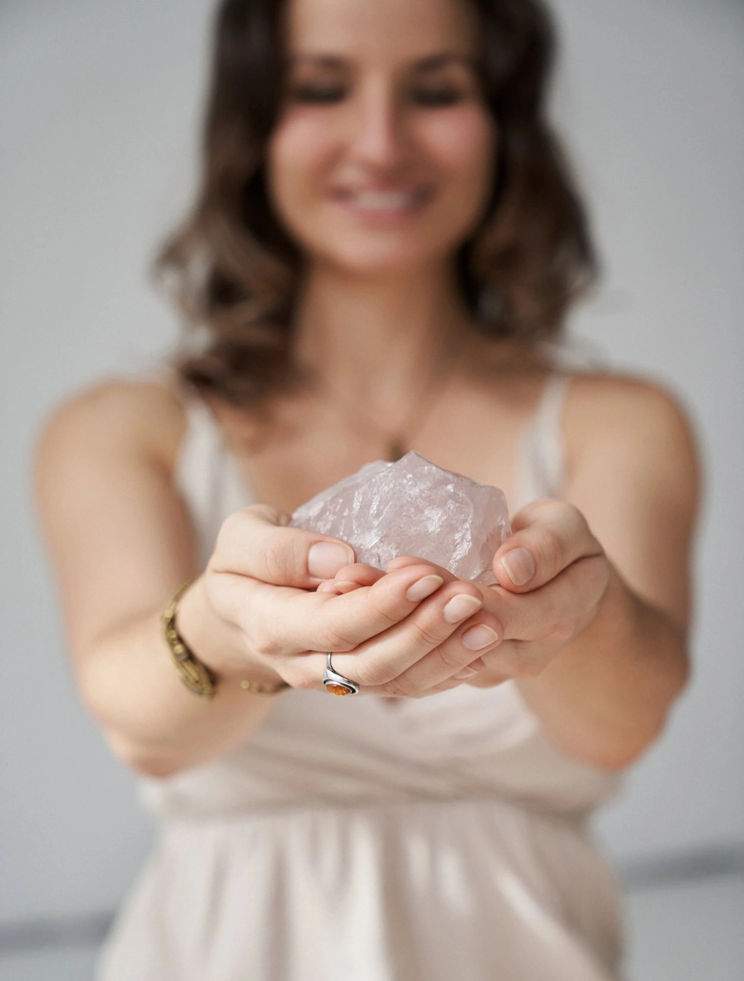 Eine lachende Frau hält einen rosa Edelstein in den Händen. Sie trägt eine goldene Uhr und einen Ring am rechten Finger.