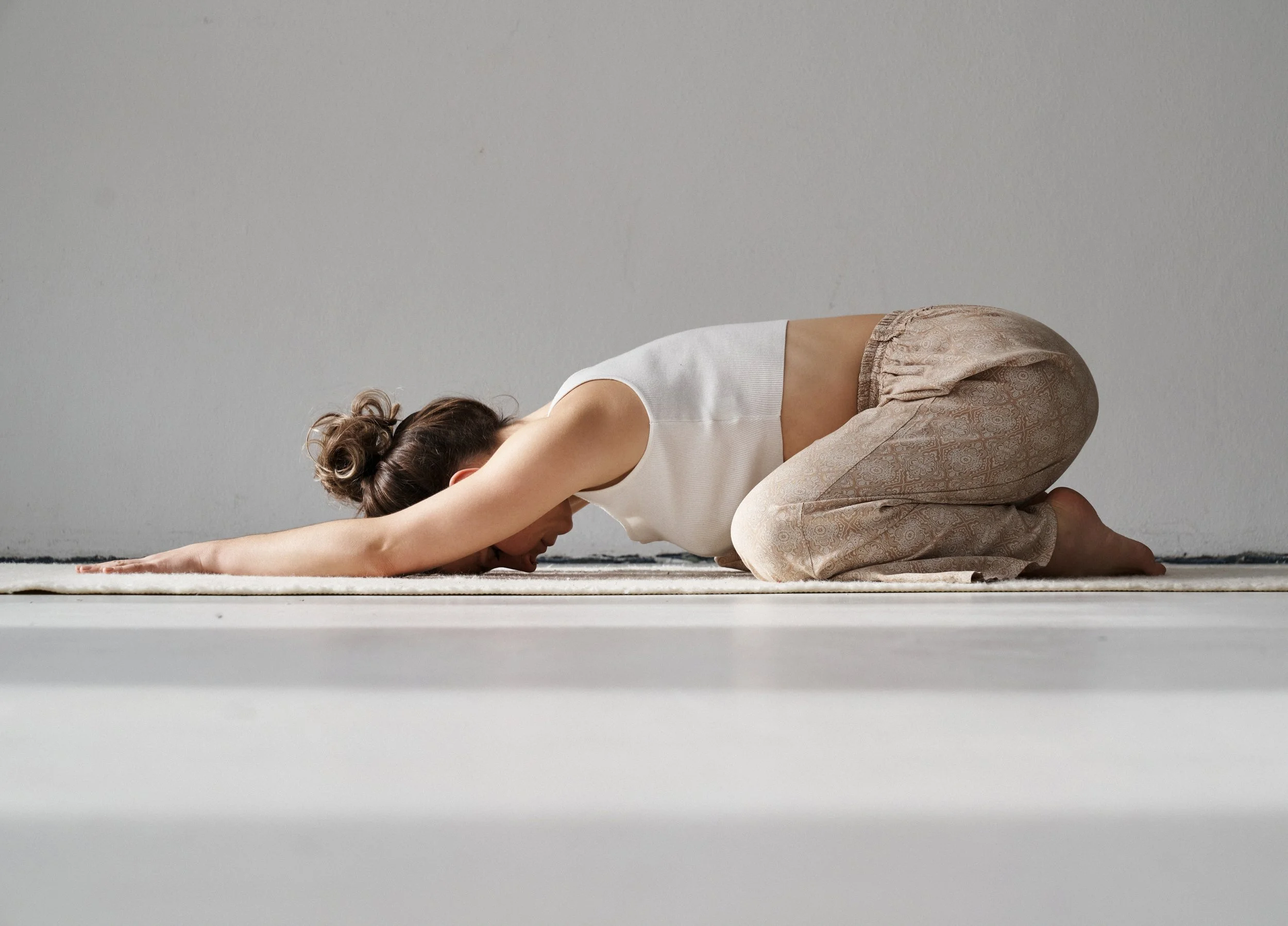 Franziska Riedl, Yoga Lehrerin macht die Kindhaltung, eine Asana, auf einer Yoga Matte vor einer weißen Wand für innere Ruhe, Erdung und Entspannung für das Nervensystem