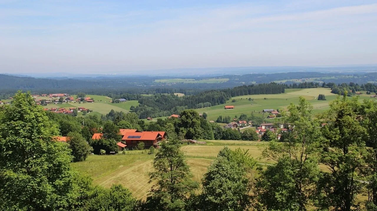 Landschaft mit grünen Hügeln, Bäumen, verstreut liegenden Häusern mit roten Dächern und weitem Himmel für Naturverbindung und Auszeit für den Geist und Verstand, Zeit für Kundalini Yoga Wochenende in der Natur