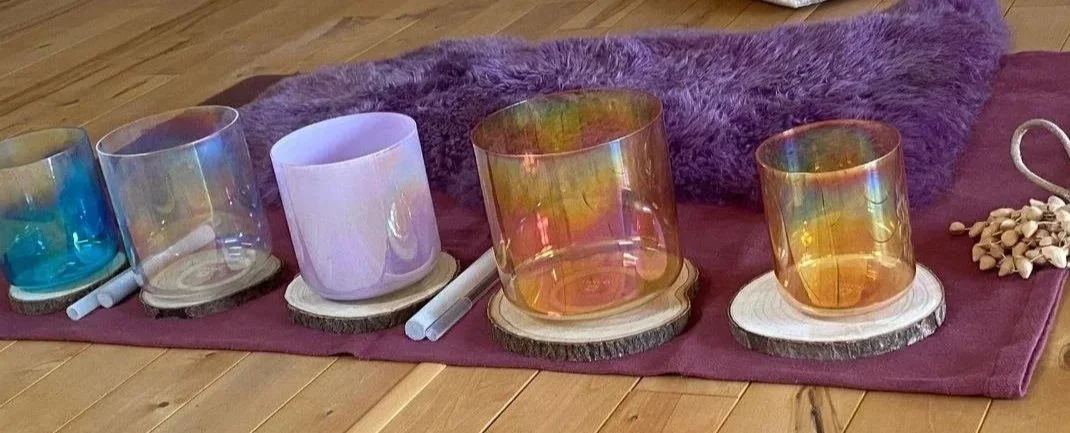 Fünf bunte Gläser aus Glas auf Holzscheiben, auf einem lila Stoff, mit Wolldecke im Hintergrund.