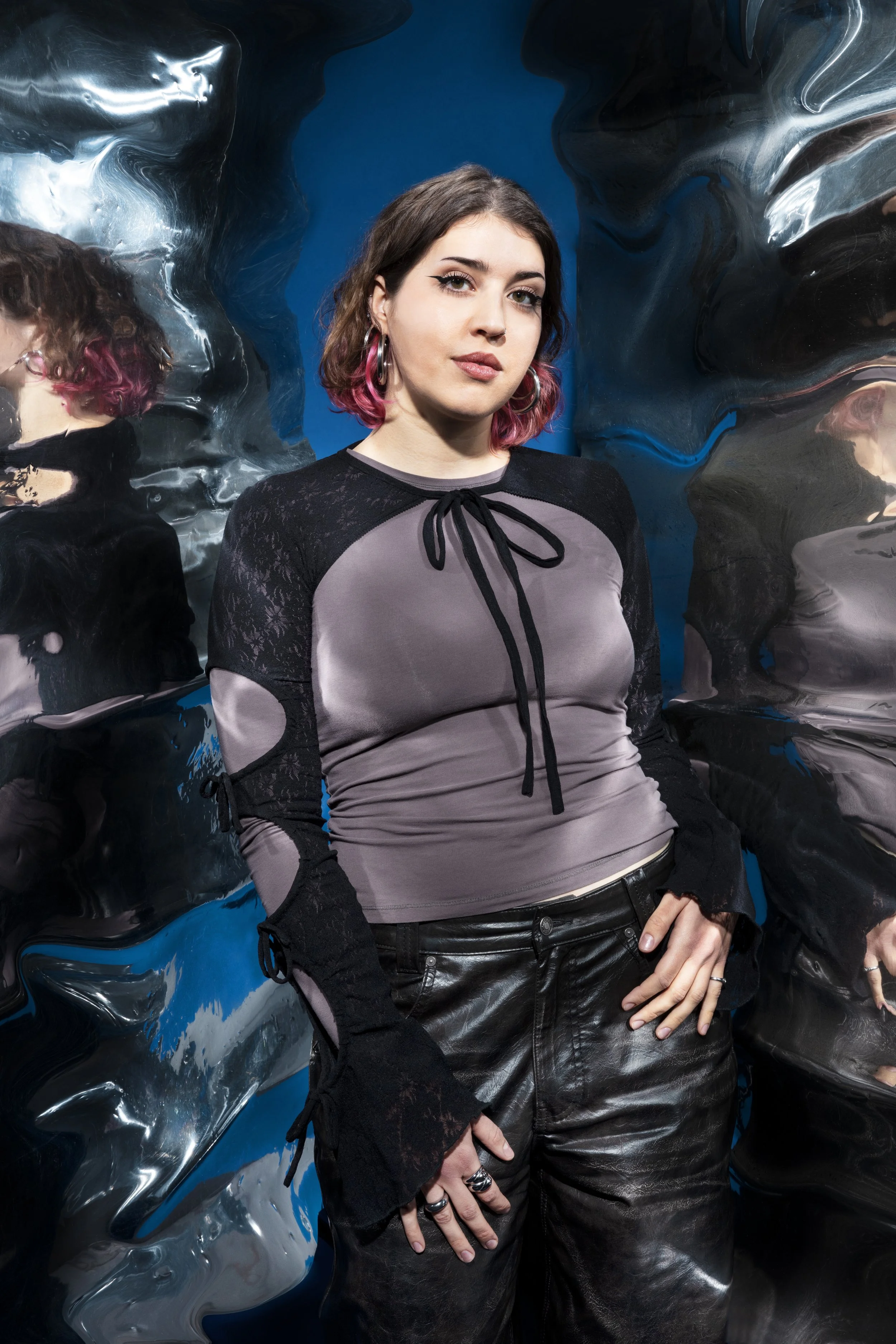 Een jonge vrouw met schouderlange haar, deels roze gekleurd, poseert voor een kunstmatige, gemanipuleerde spiegelachtige achtergrond.