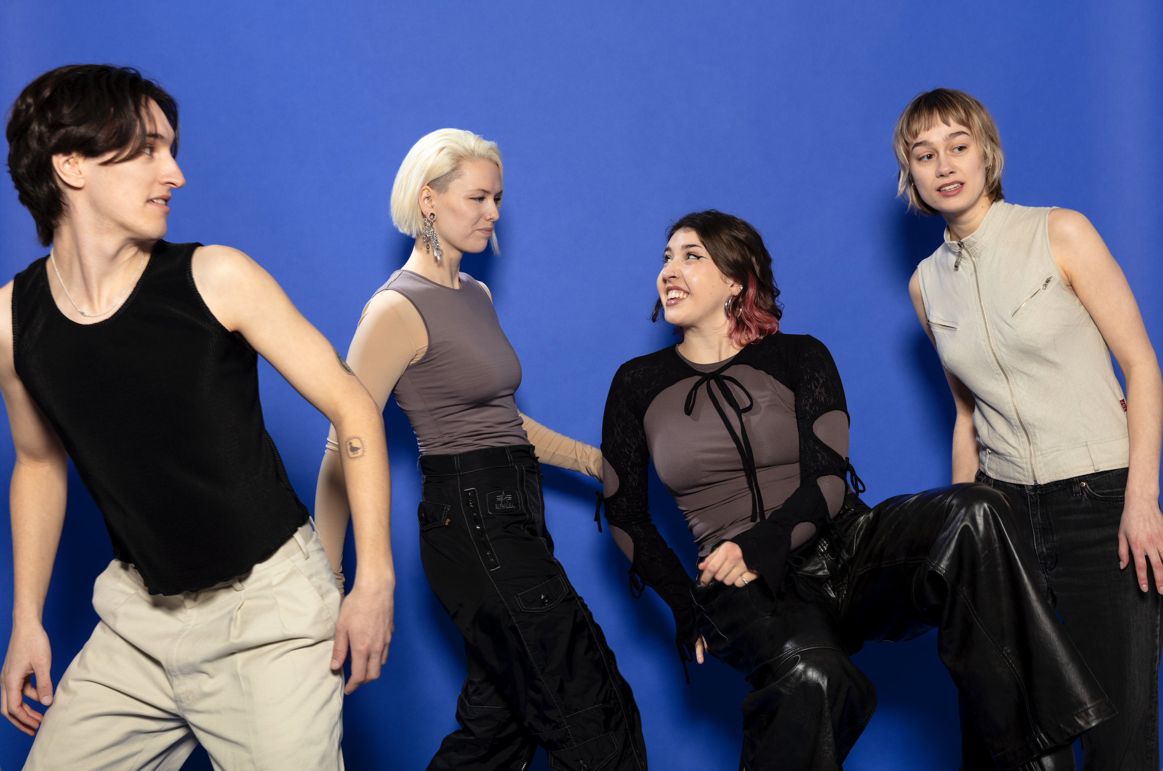 Vier jonge vrouwen poseren en lachen samen tegen een blauwe achtergrond.