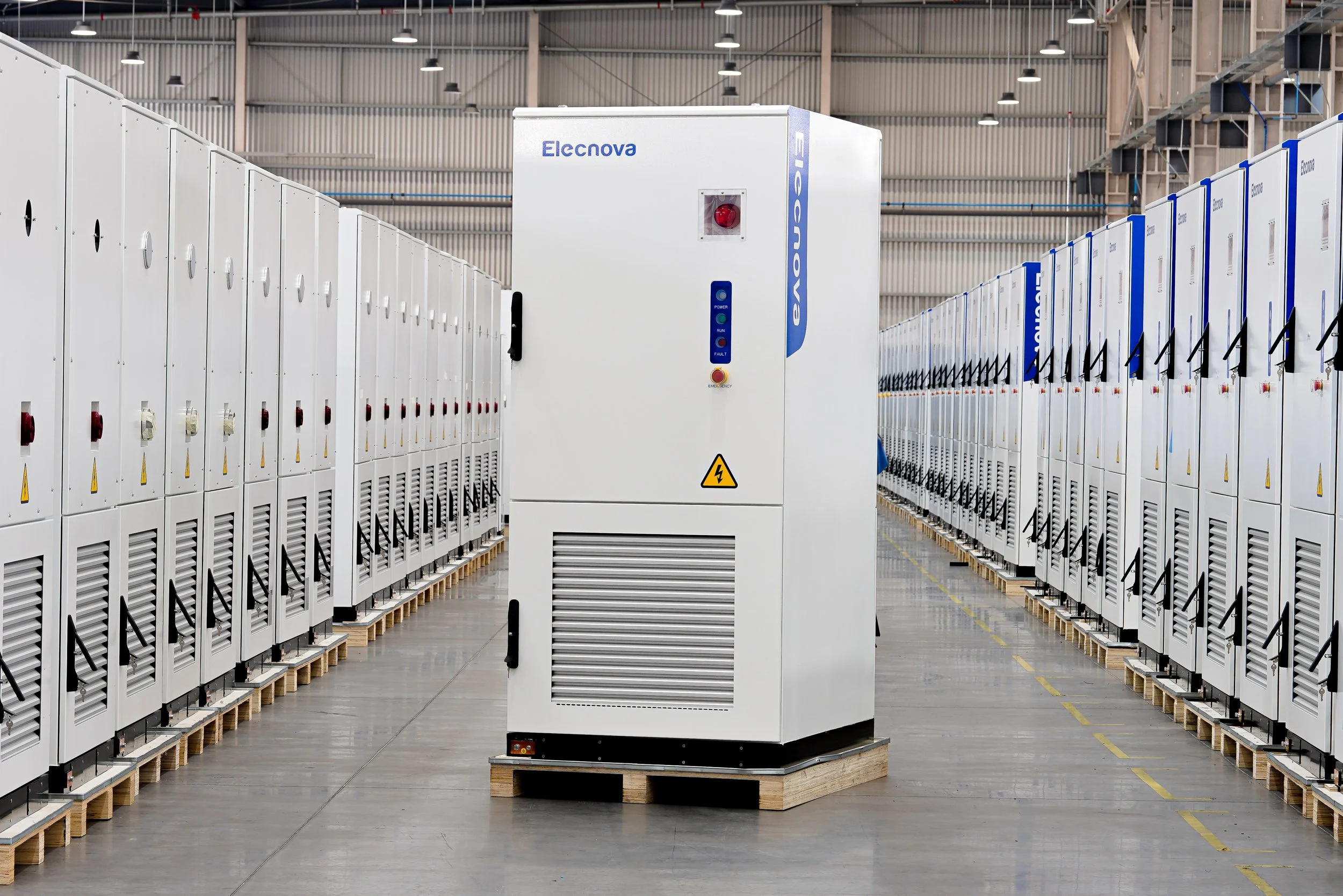 Industriebetrieb mit zahlreichen Batteriespeichern, die auf Paletten stehen. Im Vordergrund steht ein einziger Batteriespeicher mit der Beschriftung 'Elecnova'.